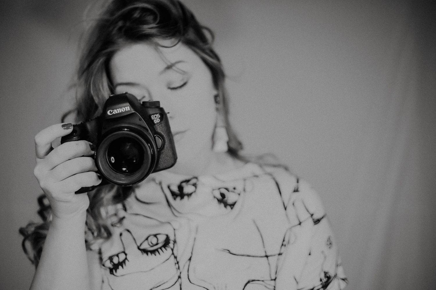 Black and white photo of someone holding a professional camera with a pattern print shirt.