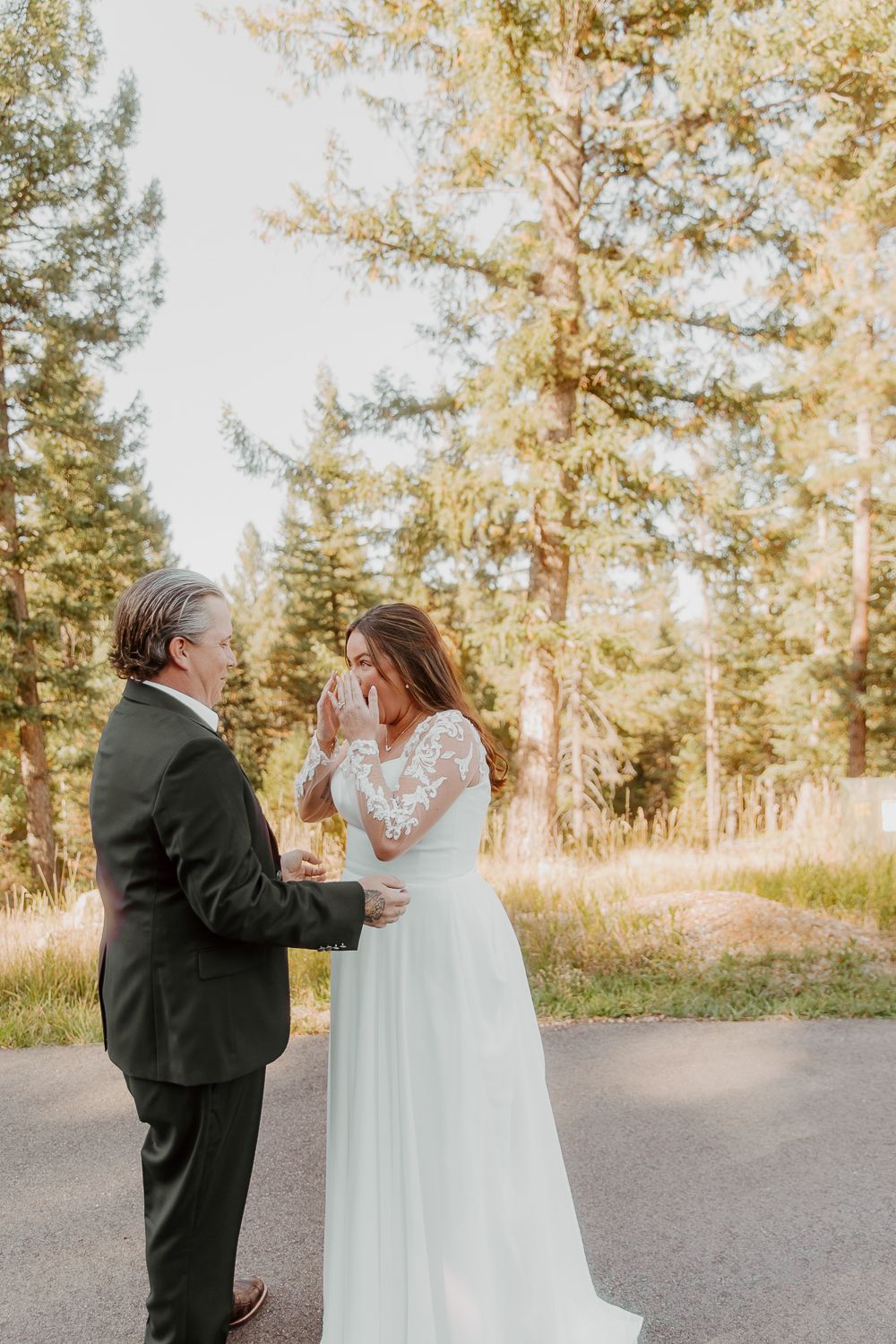 A romantic wedding moment between two people sharing a joyful reaction on a tree-lined path at sunset.