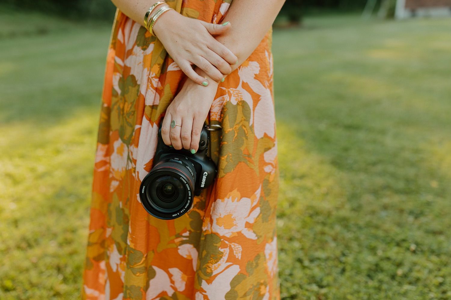 Person wearing an orange floral dress holds a black DSLR camera outdoors during golden hour.