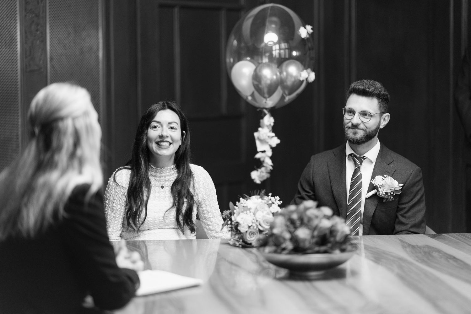 Wedding couple shares joyful laughter during their civil ceremony with heart balloon decoration and floral arrangements.