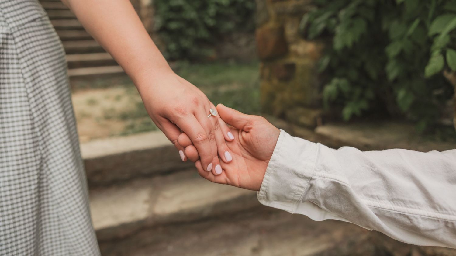 Two people holding hands on stone steps with green foliage in the background.