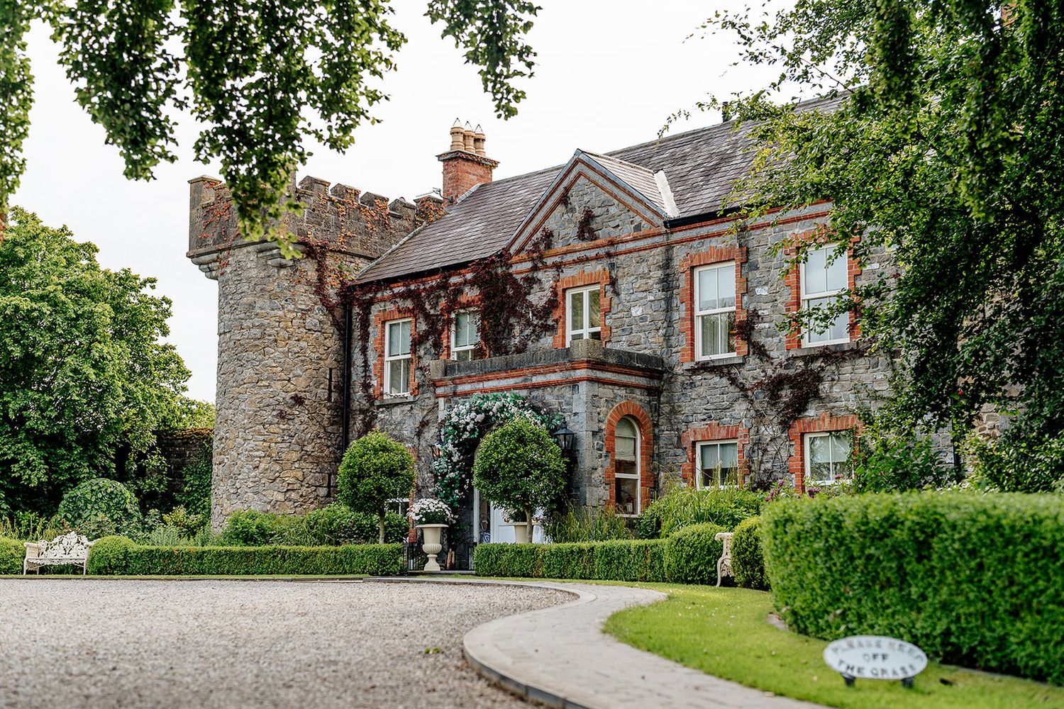 Elegant stone country manor house with decorative trim and curved driveway surrounded by manicured gardens.