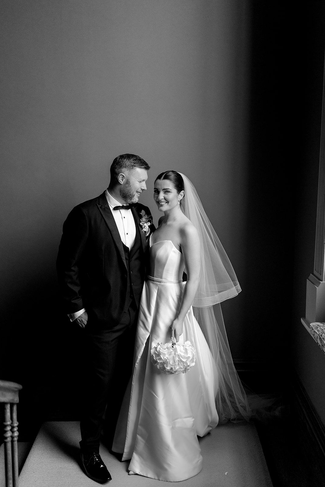 Black and white wedding portrait of newlyweds sharing an intimate moment in elegant formal attire.