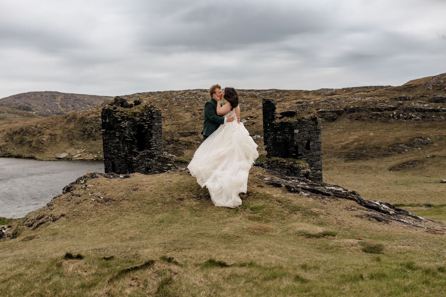 Couple embraces near historic stone ruins under dramatic cloudy sky.