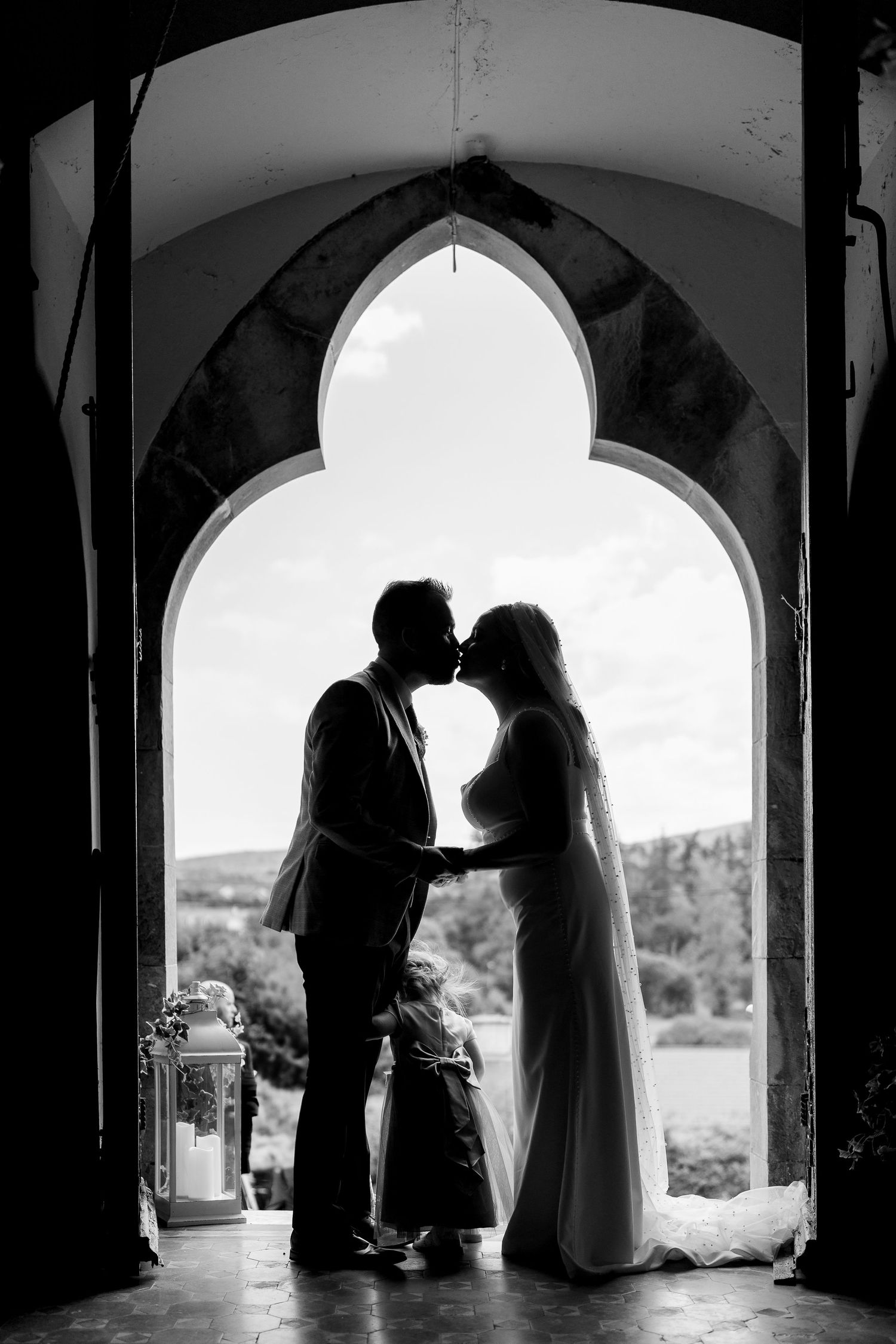 Romantic silhouette of a couple embracing in arched doorway with dramatic backlighting captured in black and white.