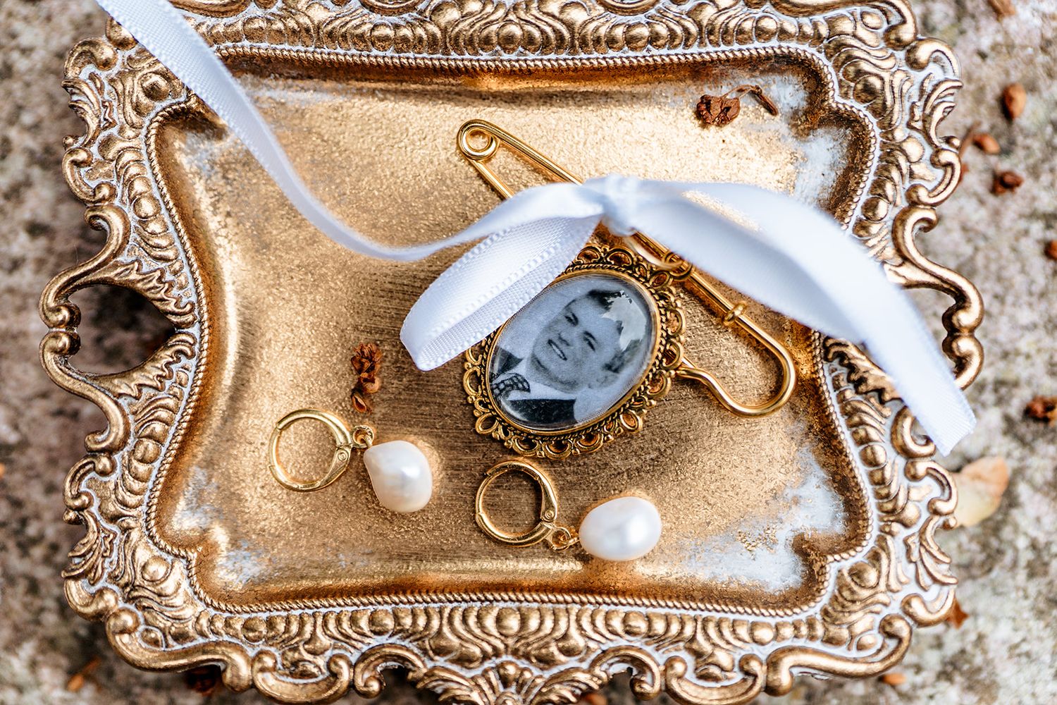 Wedding details including rings, white ribbon, and an ornate silver pocket watch arranged on a vintage gold tray.
