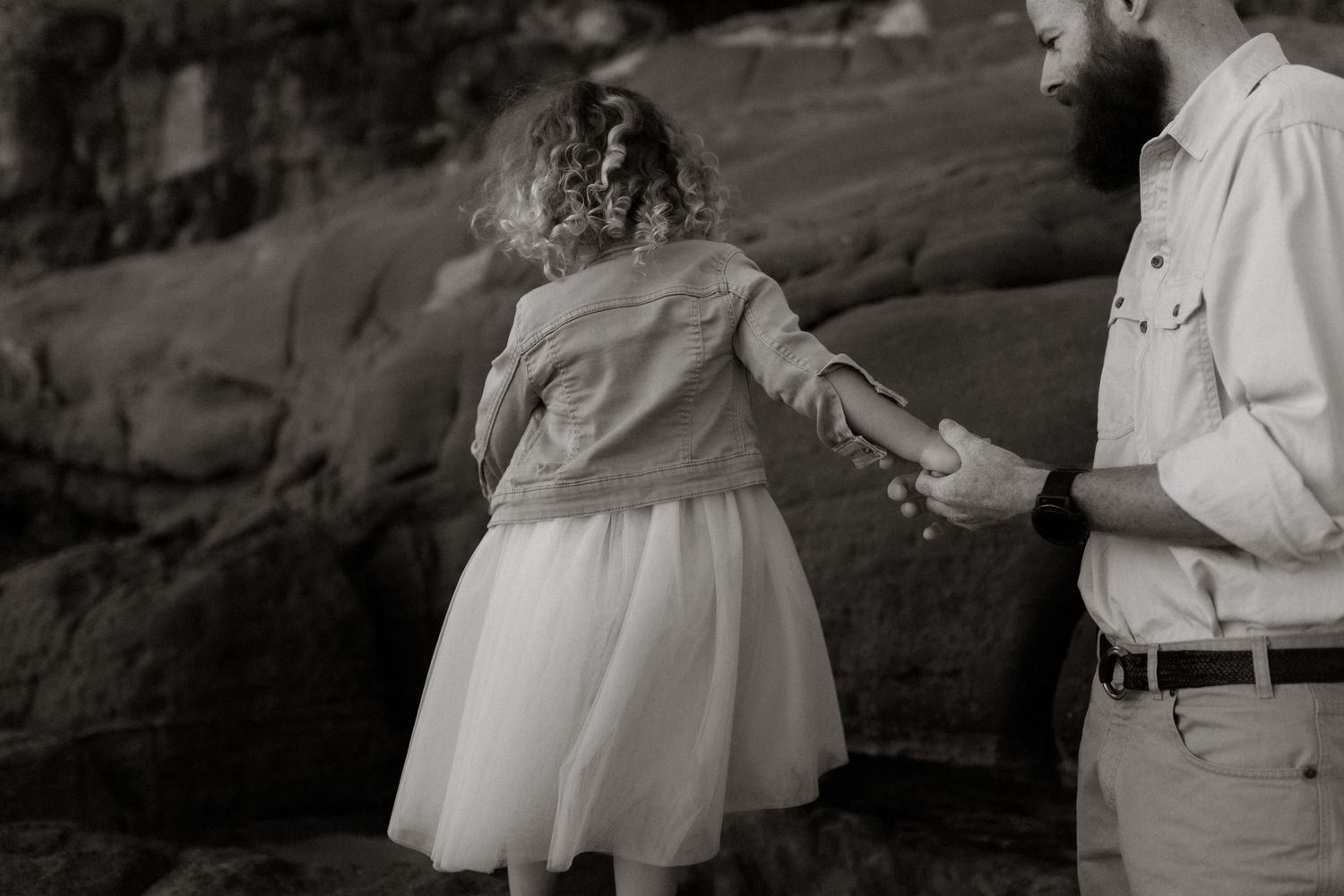 Dad holding daughter's hand to help her walk on the rocks at the beach
