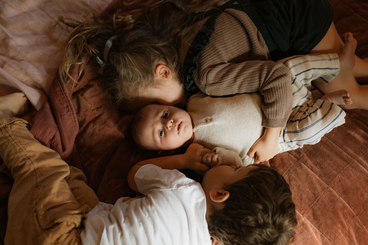 Siblings cuddling their new baby brother on the bed in their home
