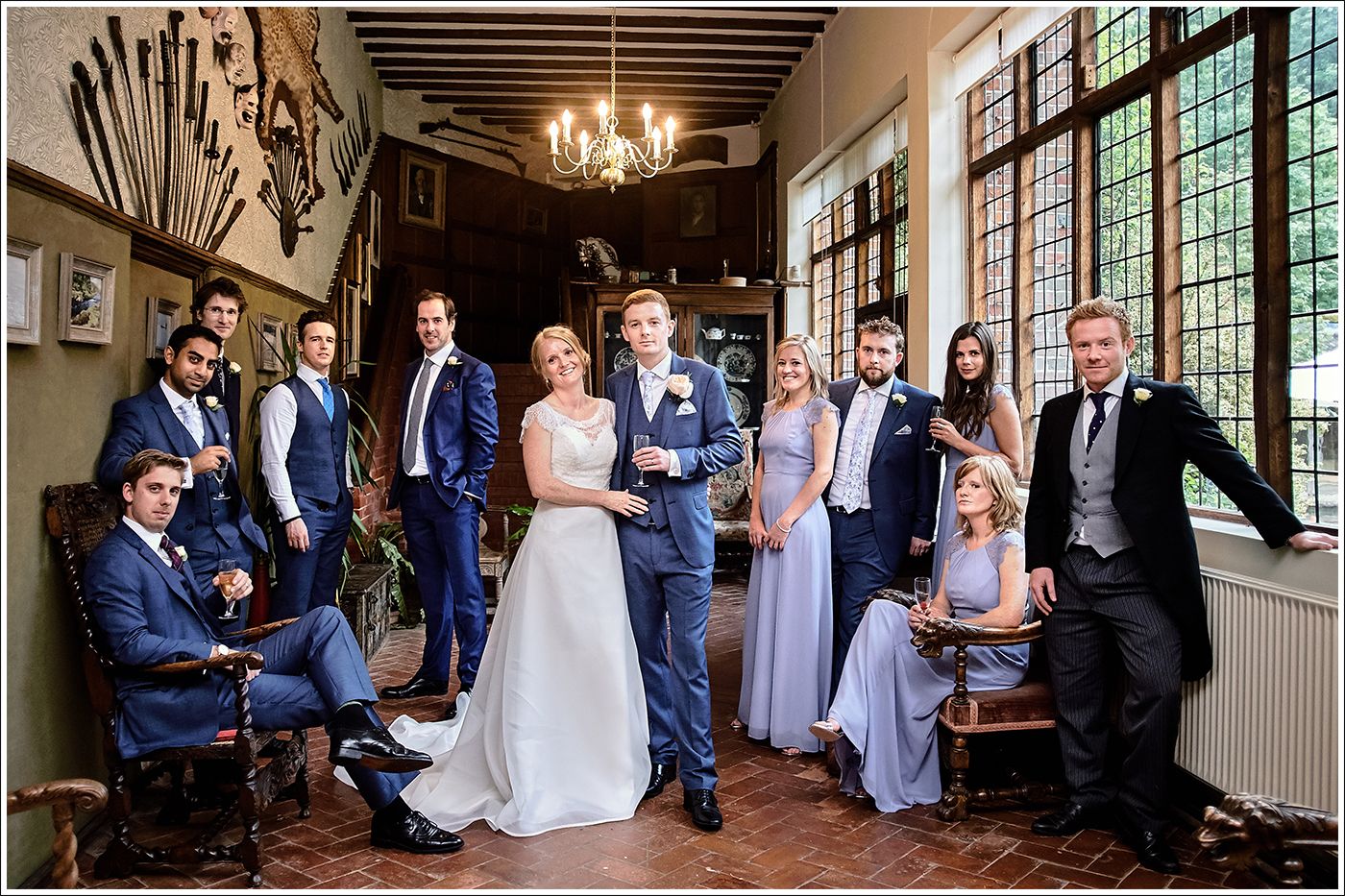 Elegant wedding party poses in Ramster Hall a rustic venue with exposed beams, chandelier and vintage decor, By Surrey Wedding Photographer