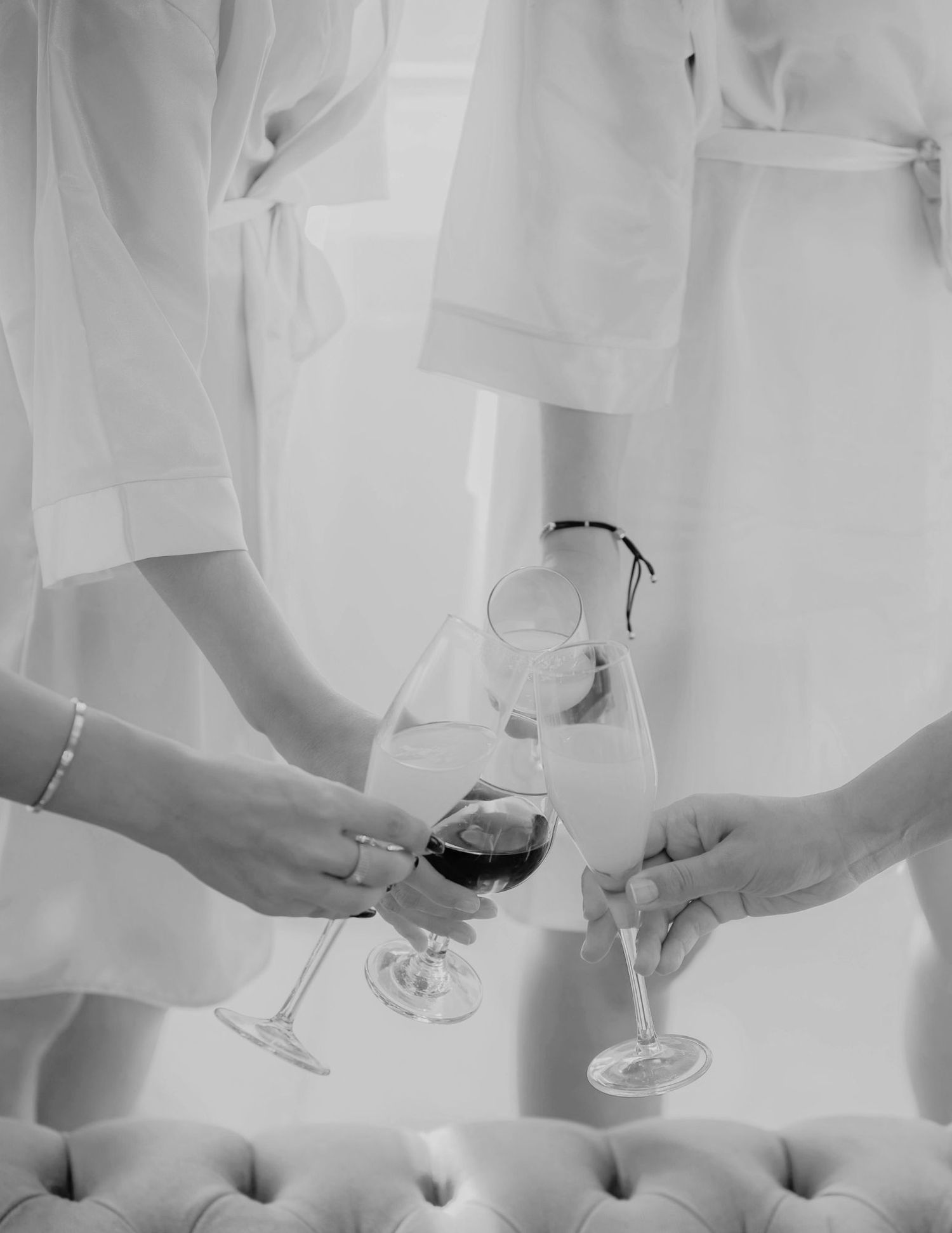 Black and white photo of hands toasting with wine glasses while wearing flowing white robes.