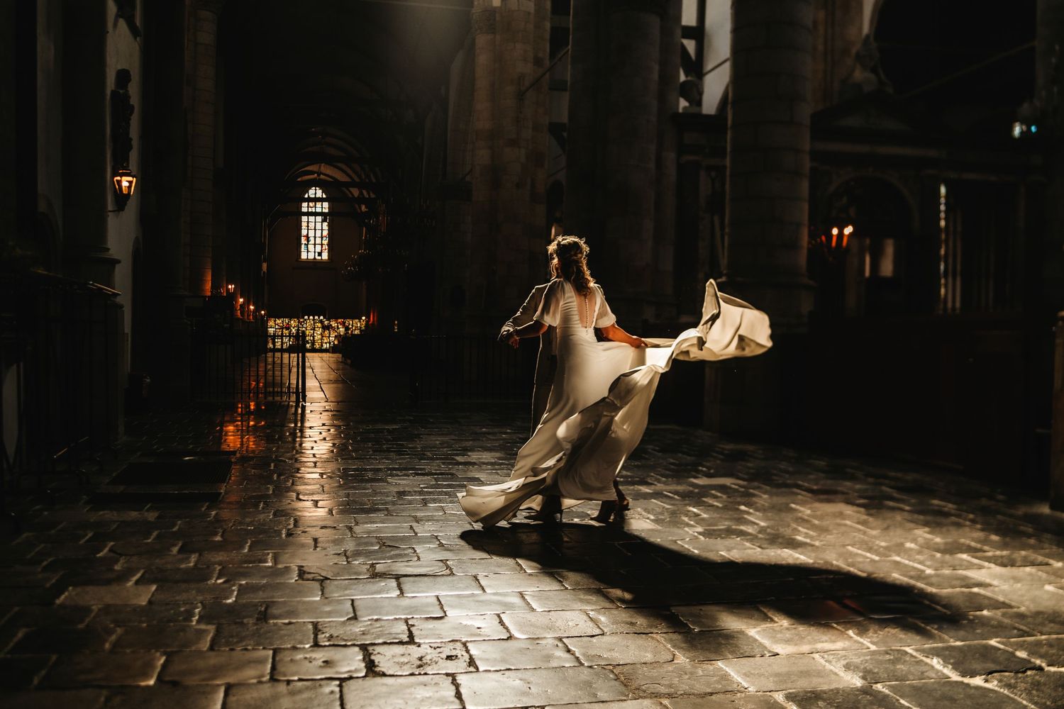 Dramatic night wedding dance photo on wet cobblestone street with cathedral backdrop.