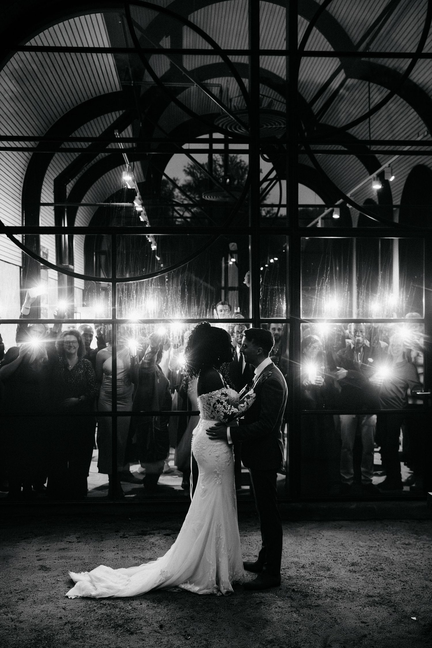 Couple shares their first dance under industrial arches with dramatic lighting and crowd silhouettes.