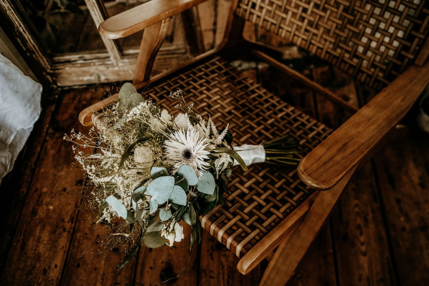 White and green floral bouquet resting on vintage wooden chair.
