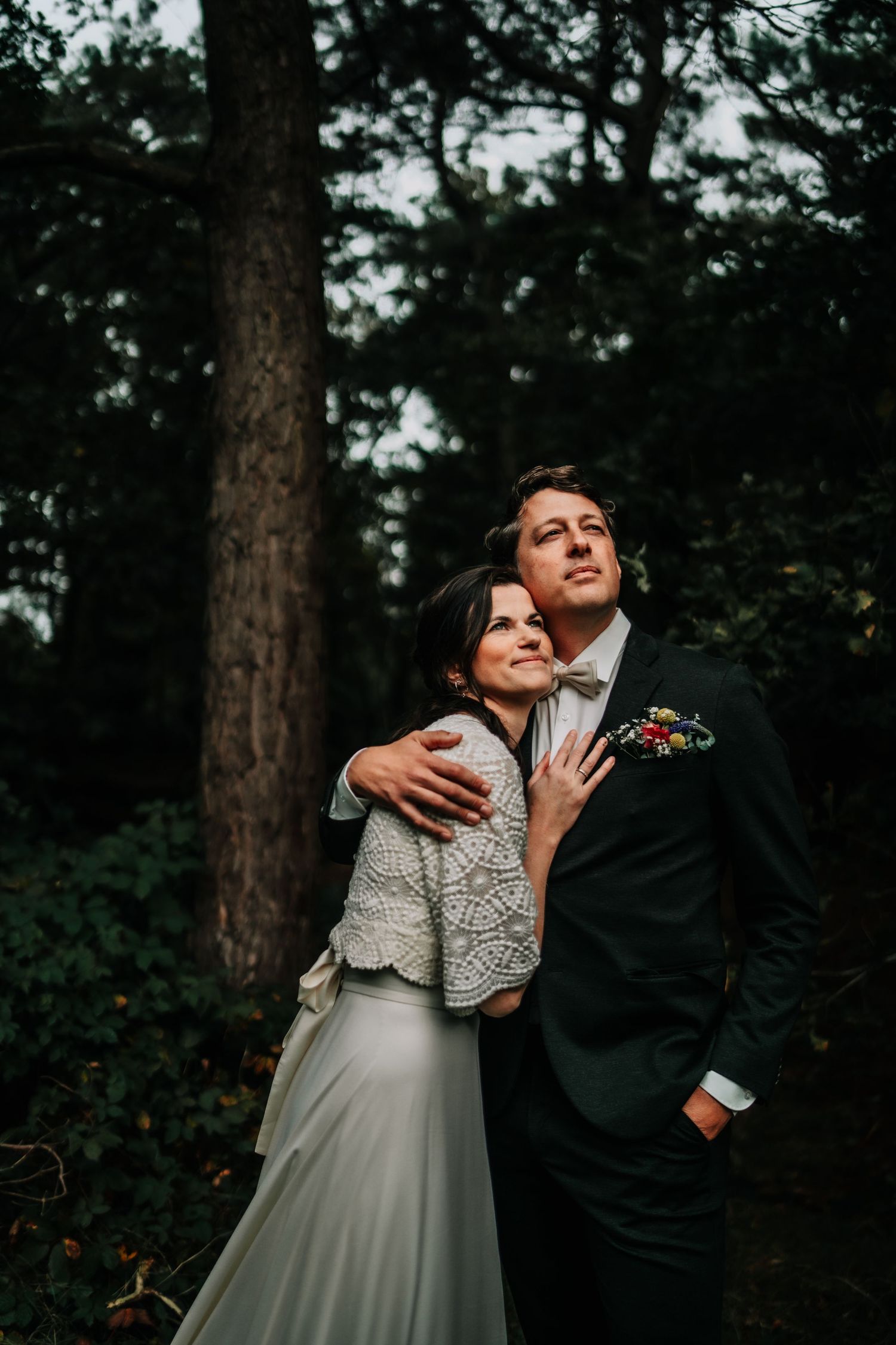 A romantic wedding portrait of a couple embracing in a moody forest setting.