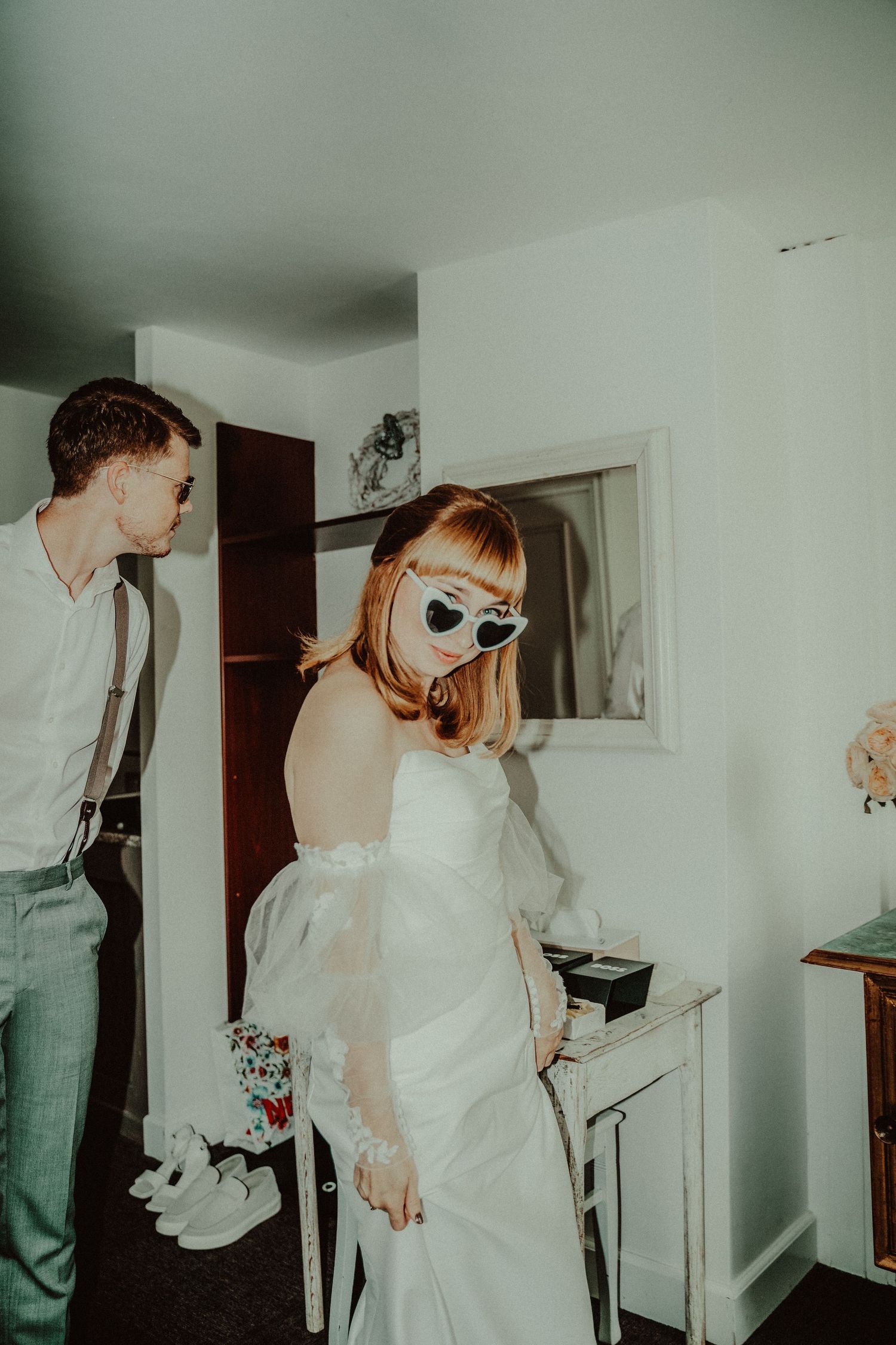 A couple in vintage-inspired wedding attire pose in a minimalist white room.