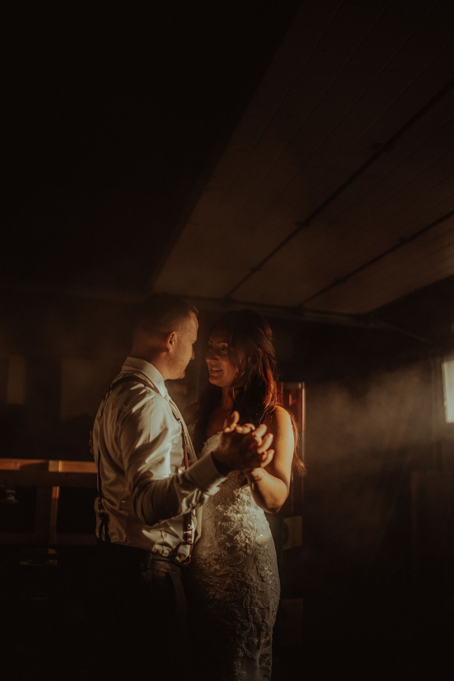 Romantic couple shares an intimate dance in a dimly lit rustic barn with dramatic backlighting and smoke effects.