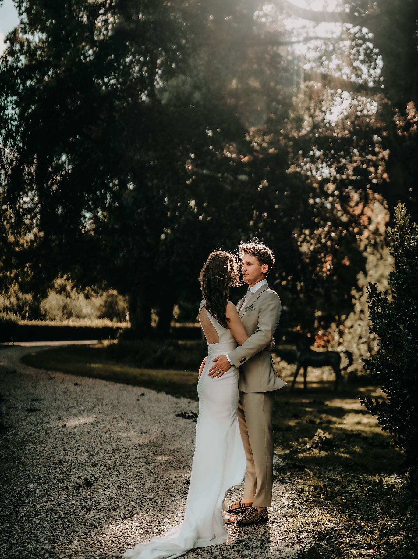 Romantic sunset portrait of newlyweds embracing on a tree-lined path.