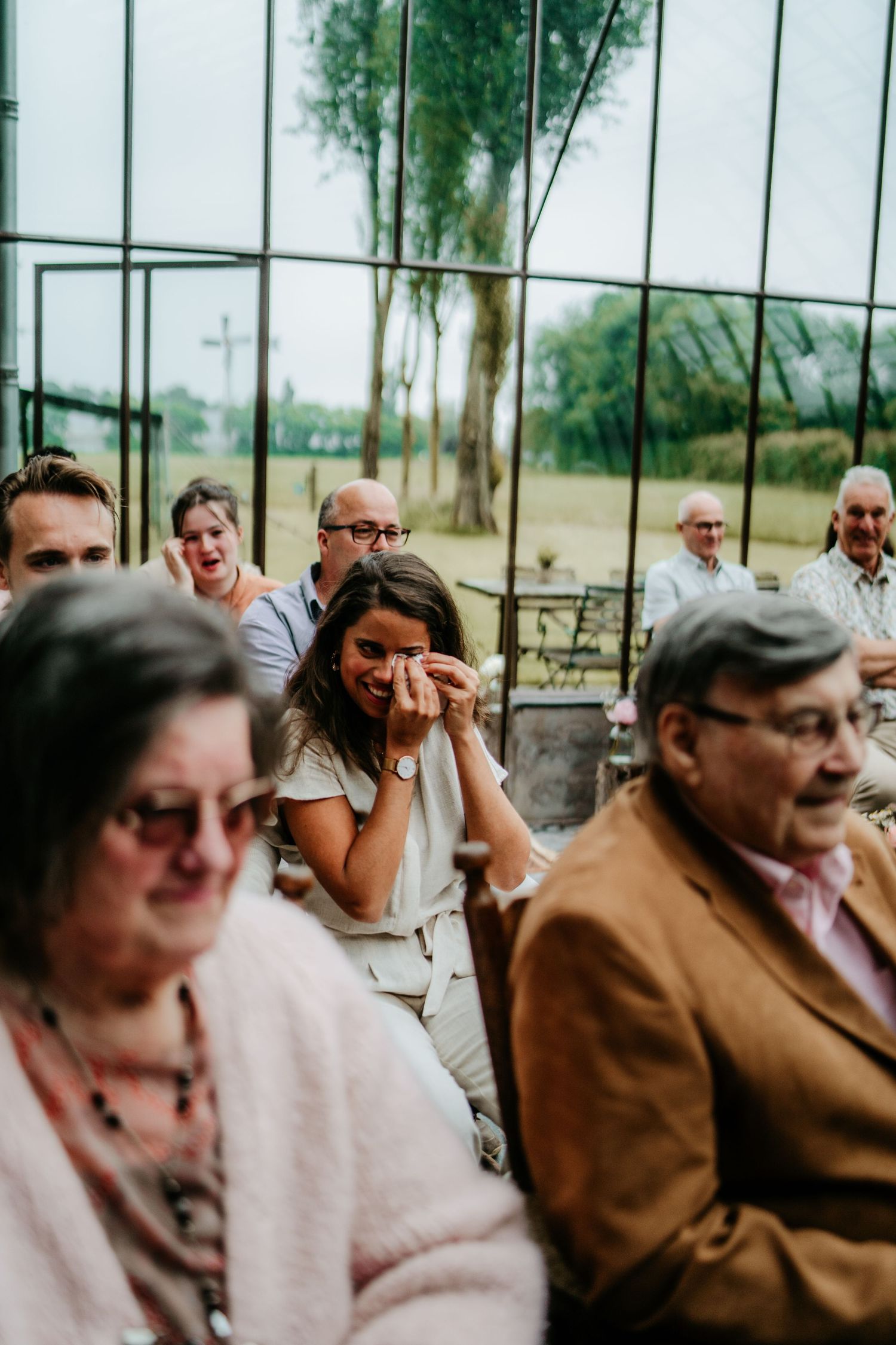 Wedding guests showing emotional reactions during ceremony with natural lighting streaming through windows.