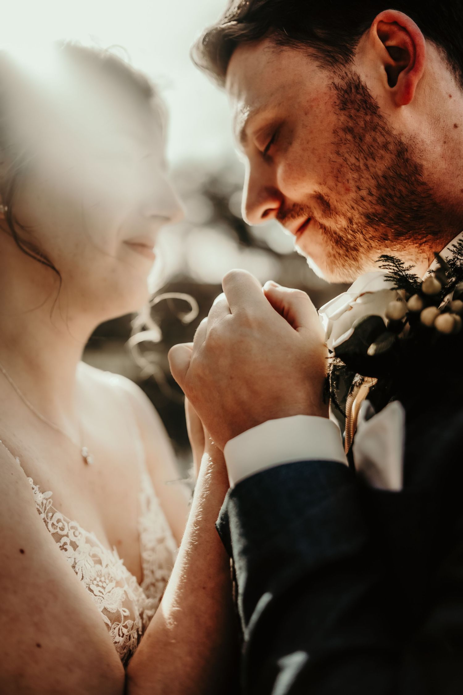 Intimate wedding moment captured in warm sunlight showing couple in formal attire sharing a tender embrace.
