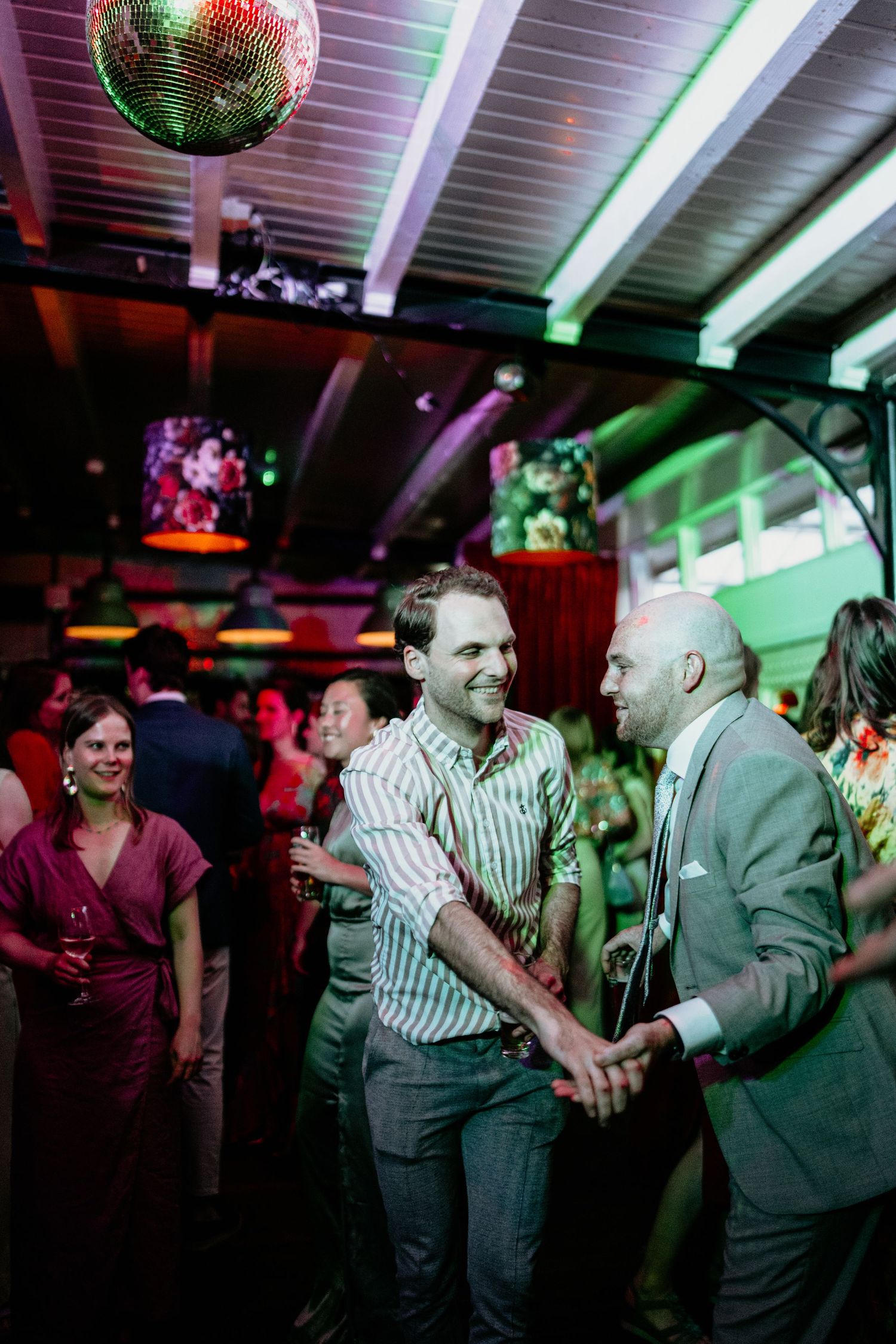 Wedding reception dance party with disco ball and colorful lighting as guests celebrate.