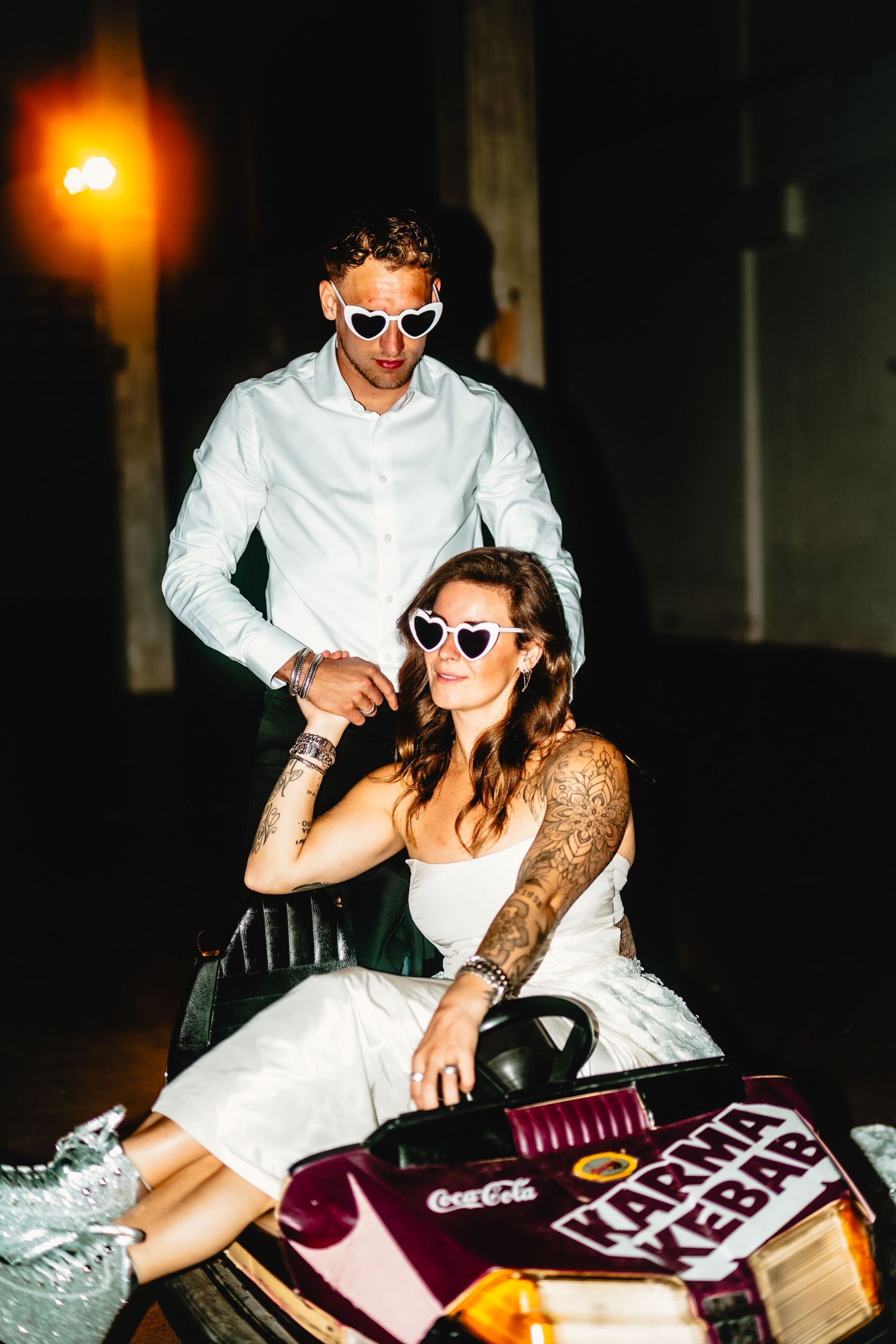 Fun wedding couple wearing matching sunglasses pose with party supplies at night.
