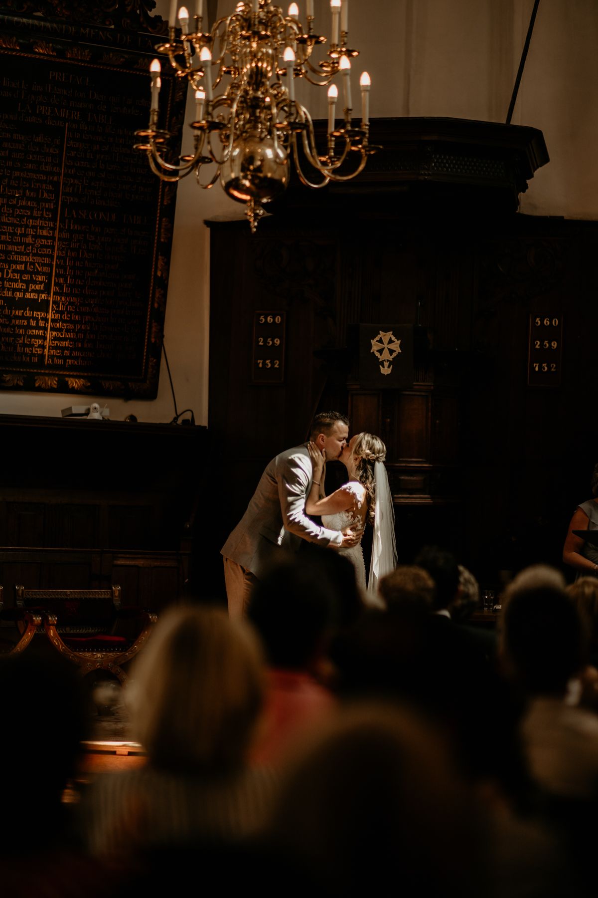 Couple shares intimate moment under chandelier during indoor wedding reception.