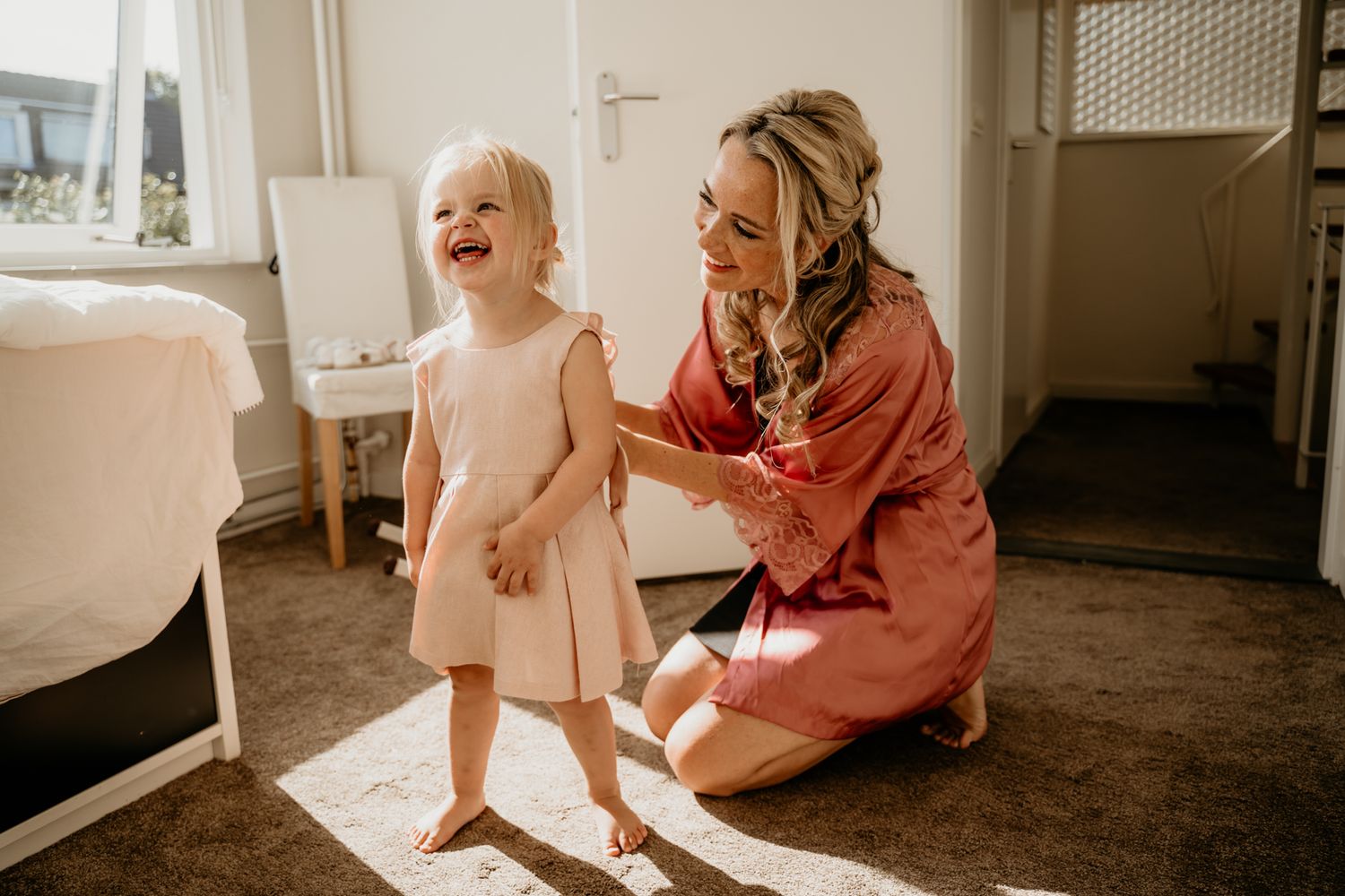 Sunlit moment of joy between child in dress and adult in coral clothing.