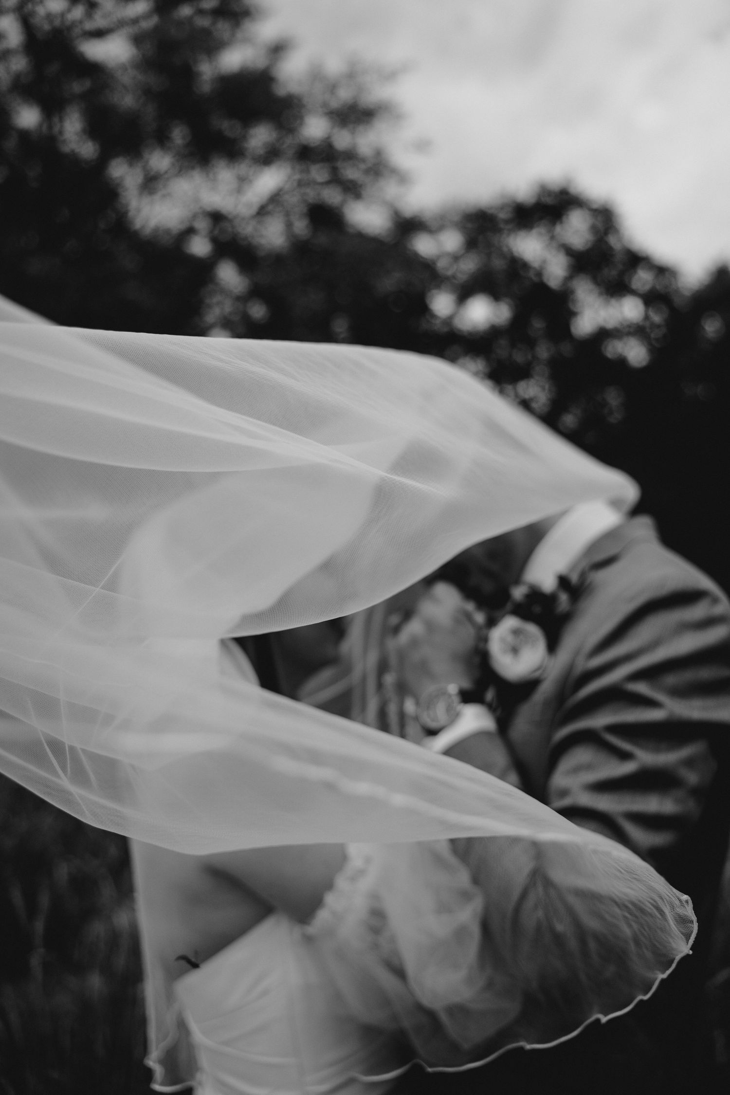 Flowing white wedding veil catches breeze in dramatic black and white photograph.