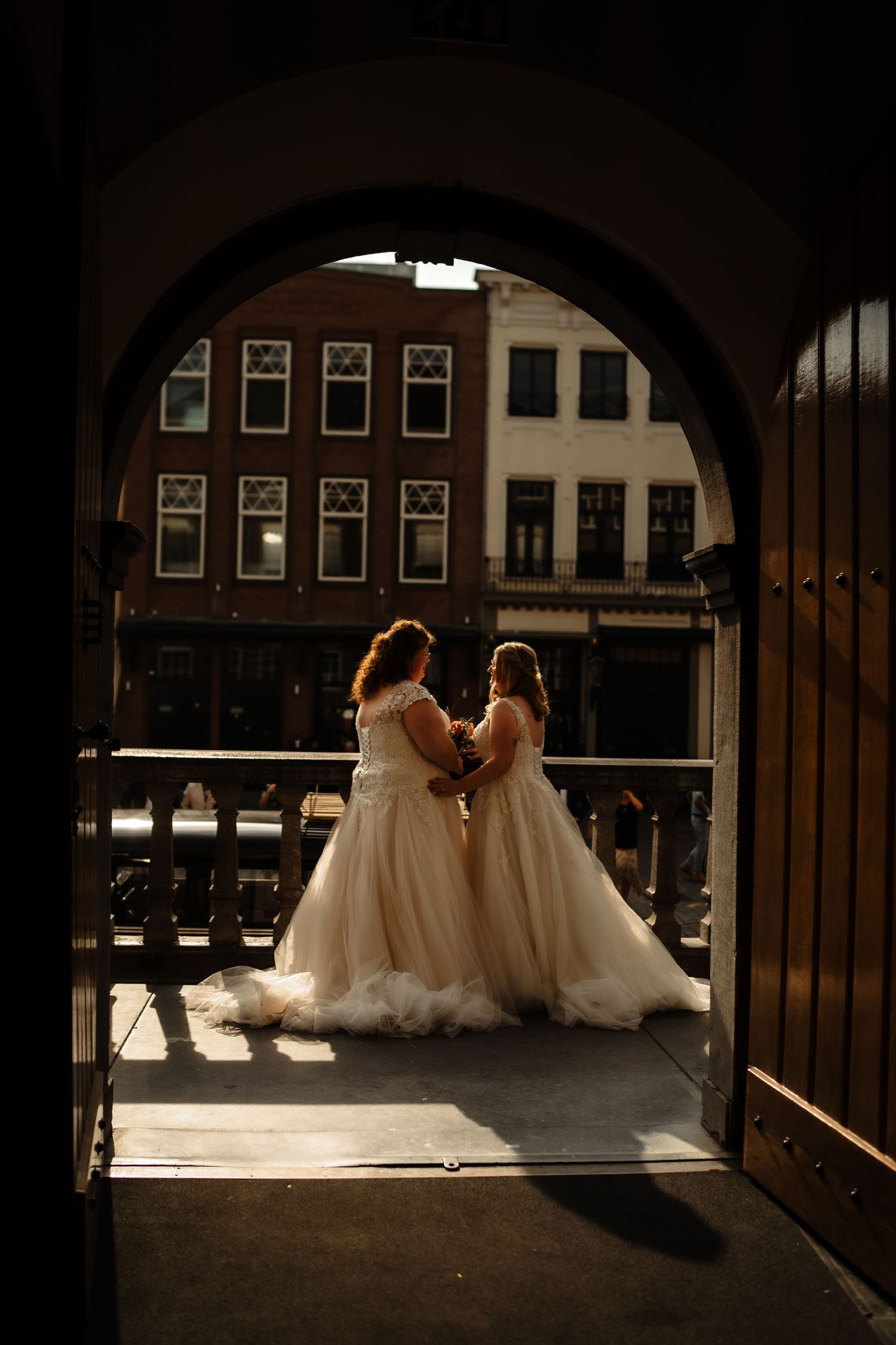 Silhouette of two brides in flowing gowns framed by historic archway.
