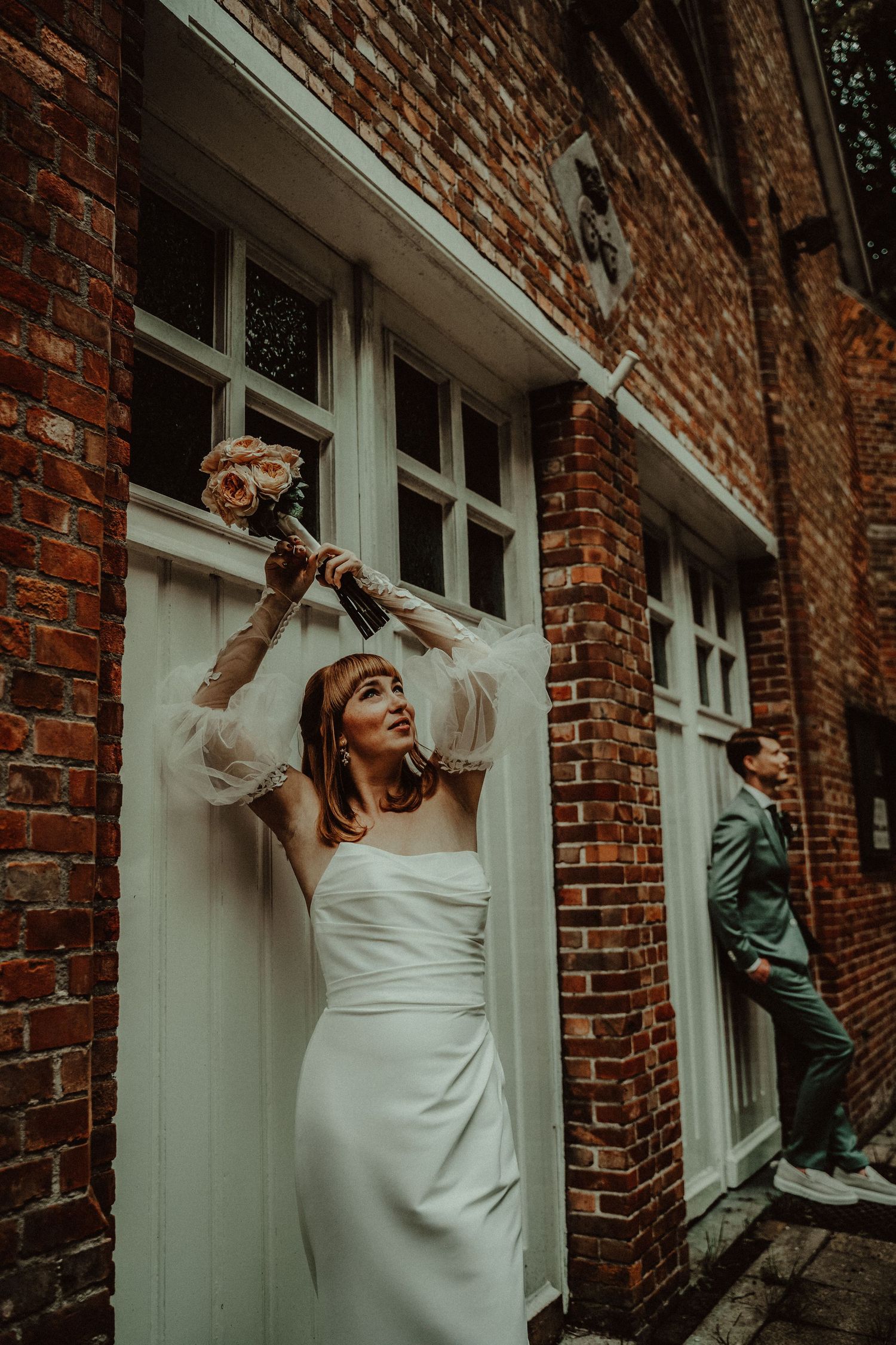 A bride poses dramatically by white doors against a rustic brick building.