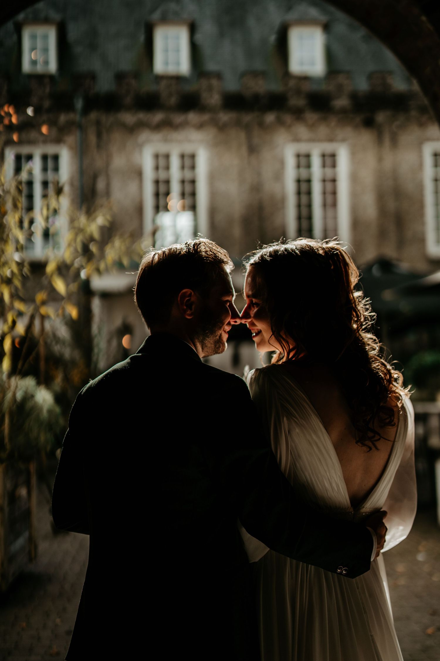 Romantic backlit portrait of couple against historic building facade at dusk.