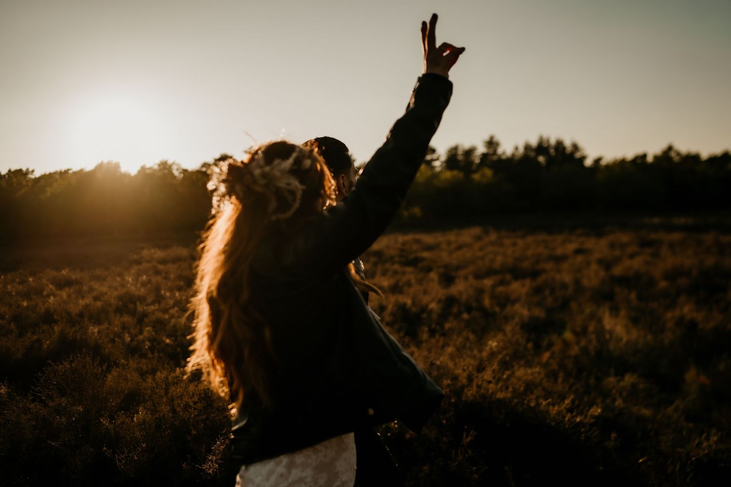 Silhouette of person with arms raised against golden sunset in field.
