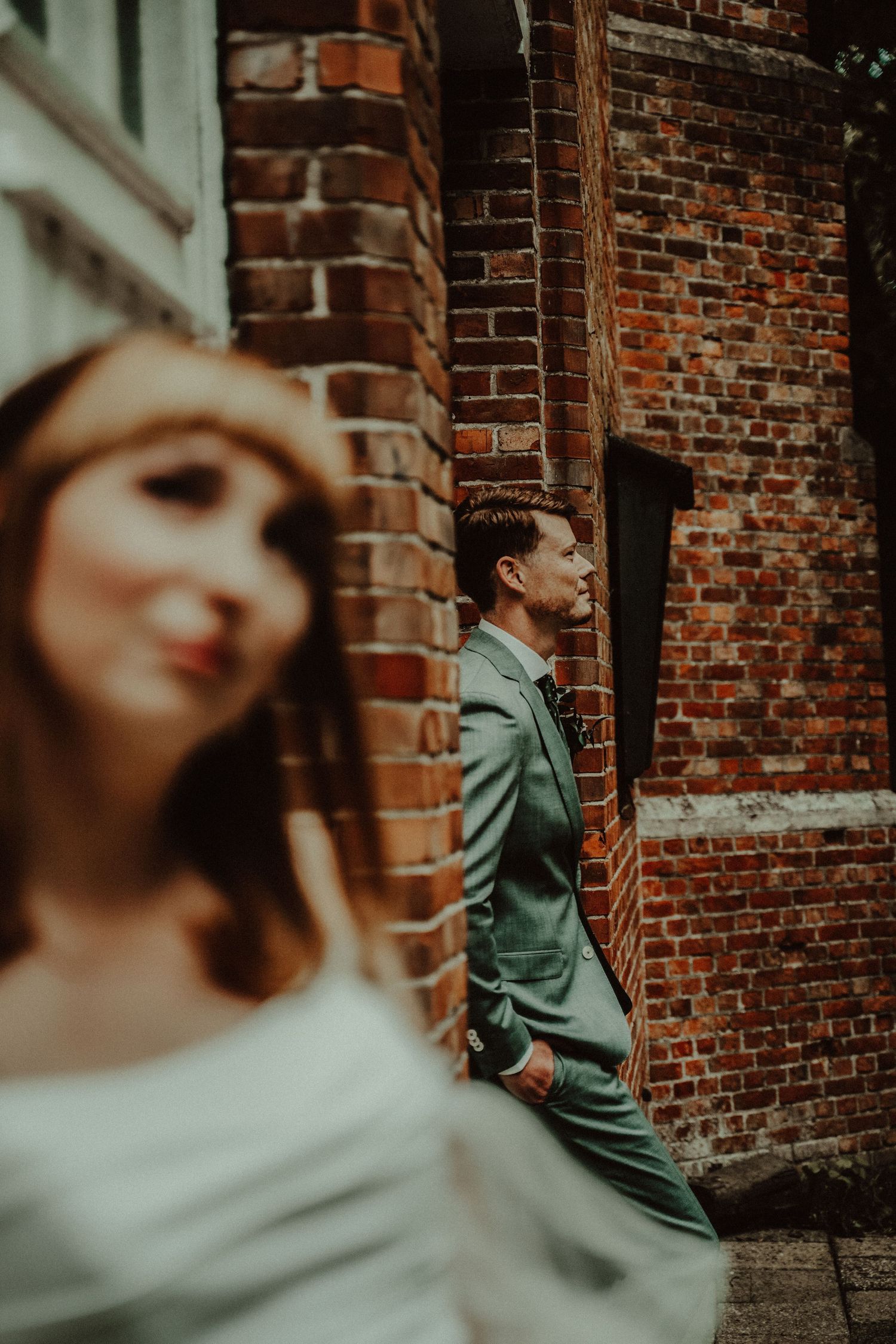 Artistic wedding portrait against rustic brick wall with dramatic composition.