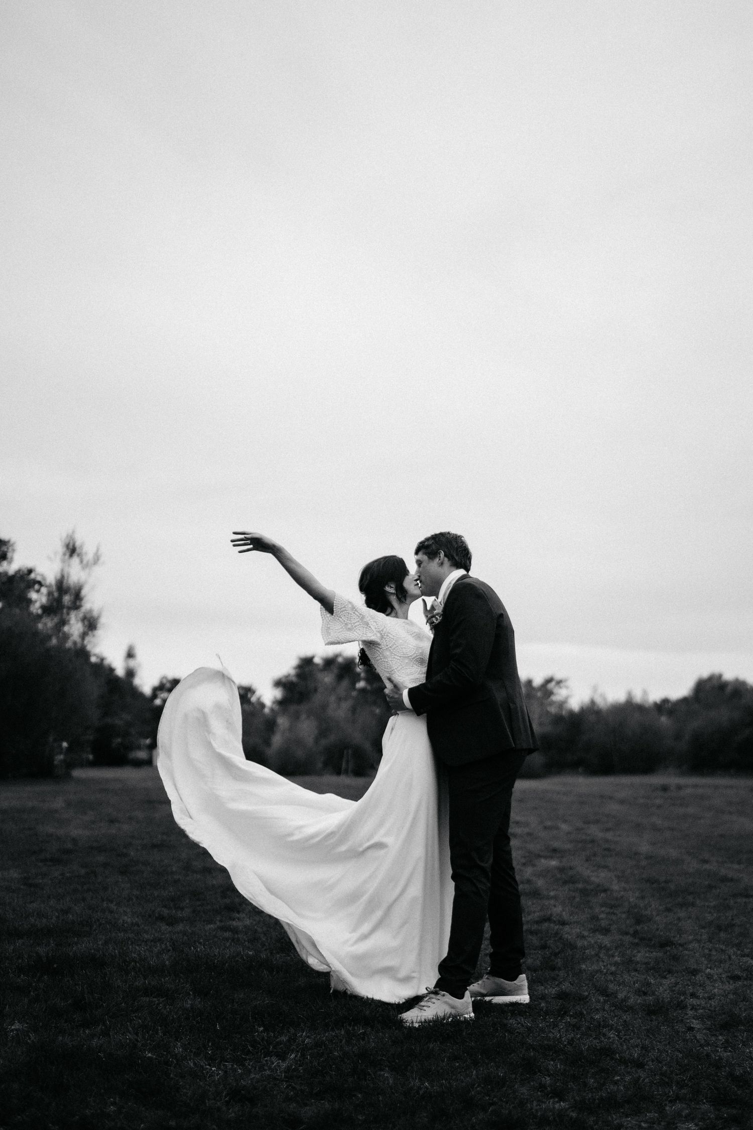 A dramatic black and white shot of a couple dancing with the bride's dress flowing in the wind.
