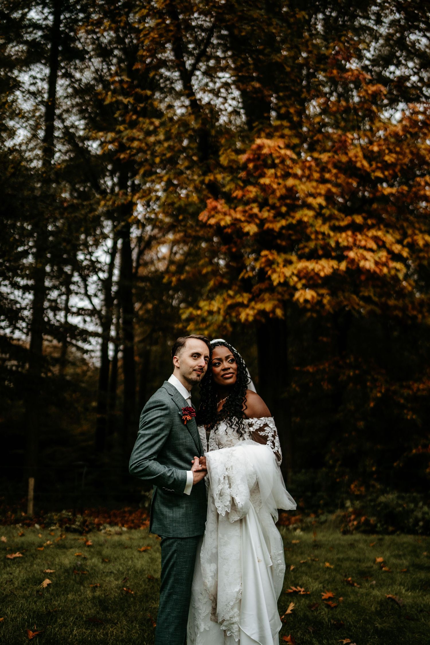 Wedding couple poses together against vibrant autumn foliage in a forest setting.