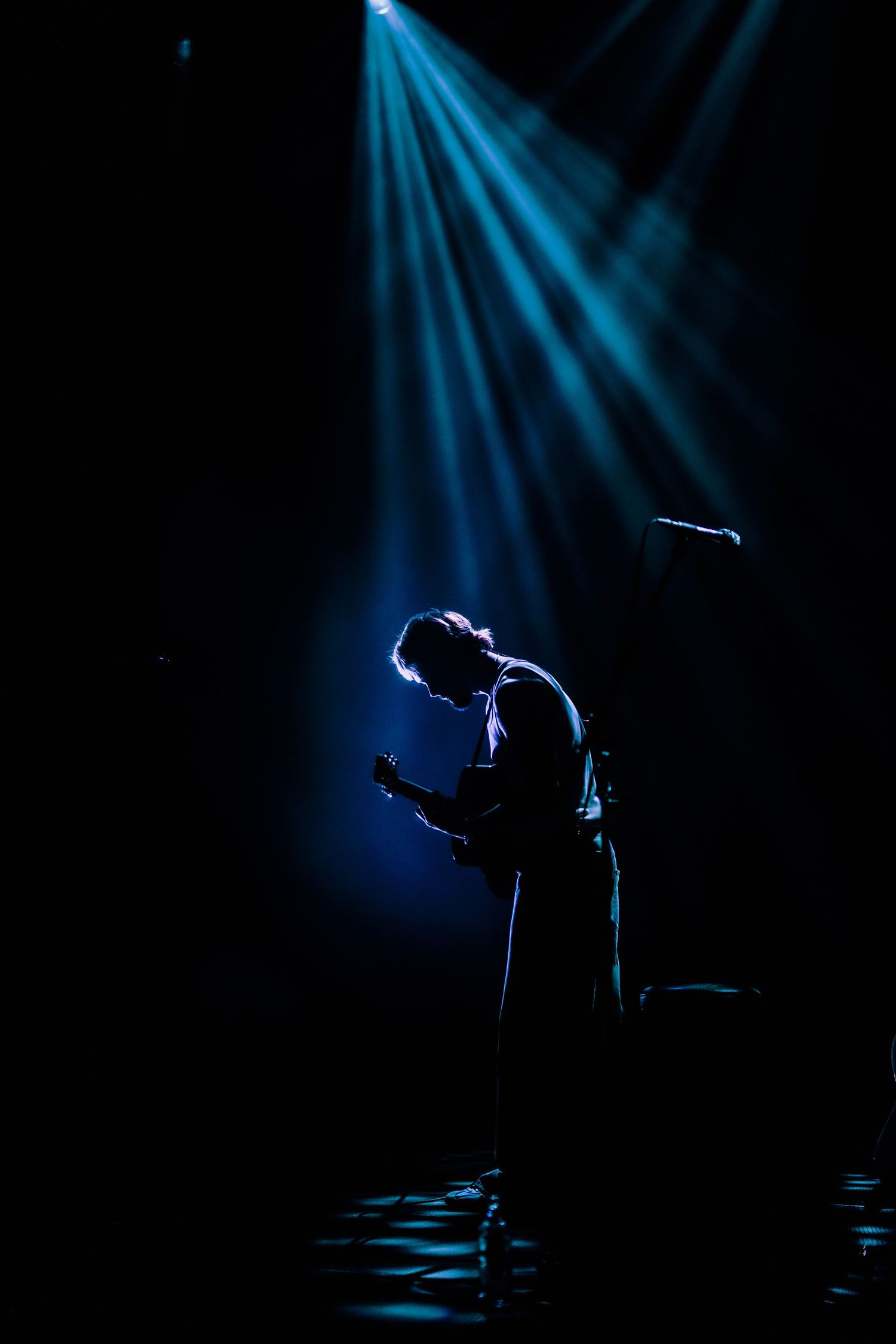 Performer silhouetted on stage under dramatic blue spotlights.