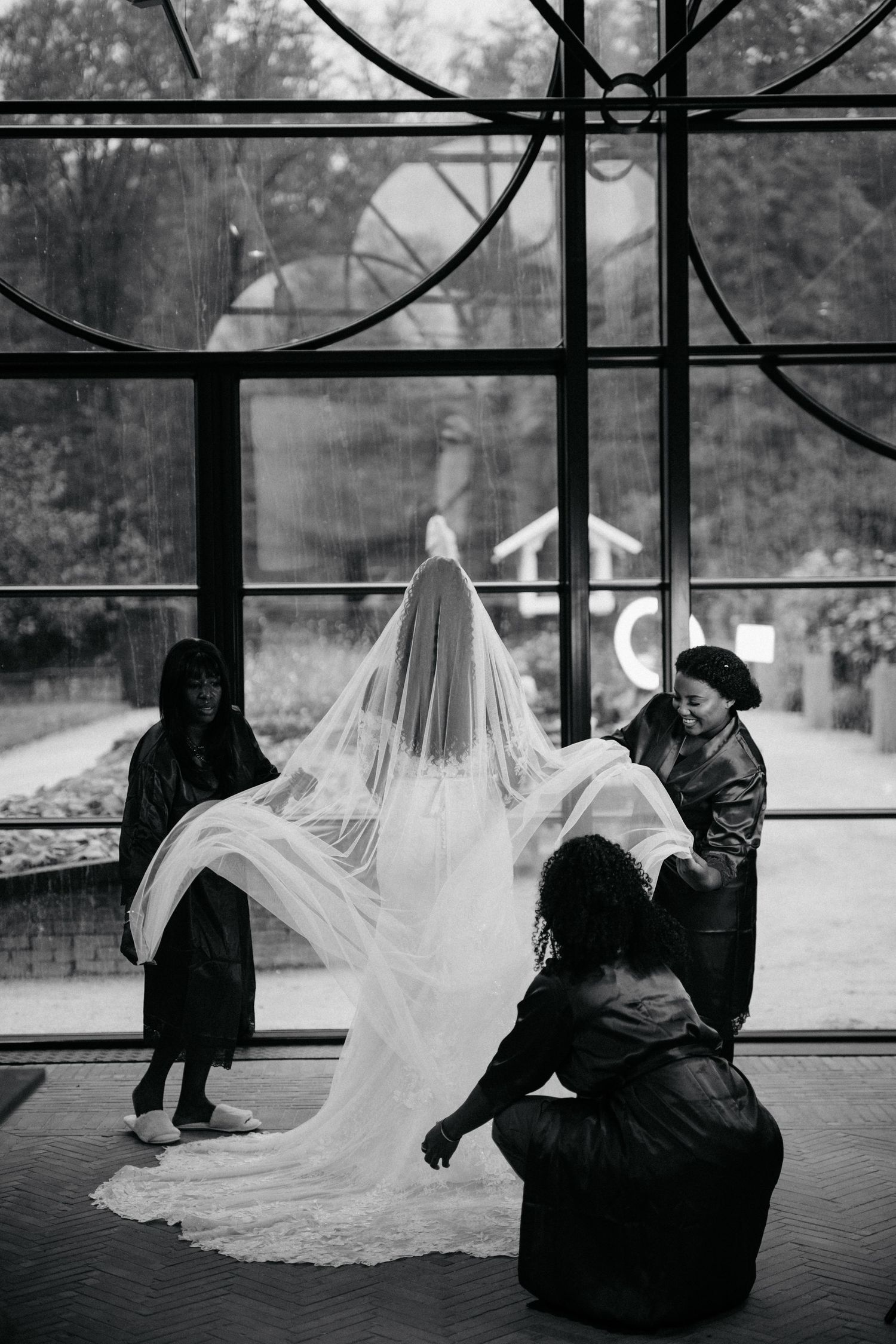 Bridesmaids adjust a flowing wedding veil in a dramatic black and white photograph.