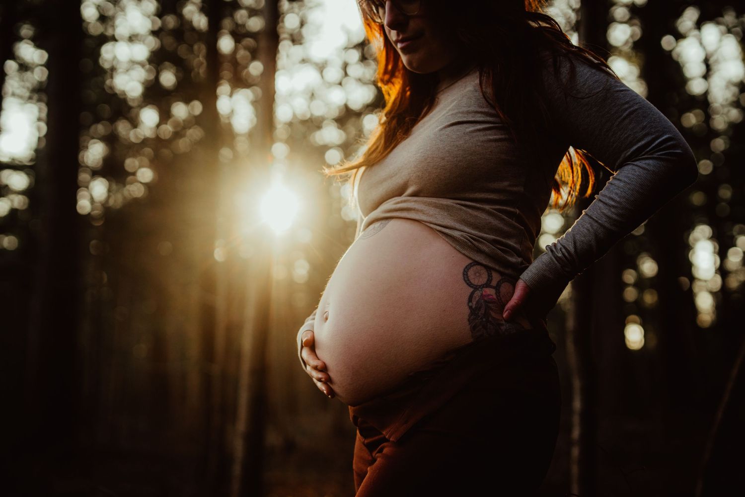 Silhouette of pregnant woman's belly against sunset in forest setting.