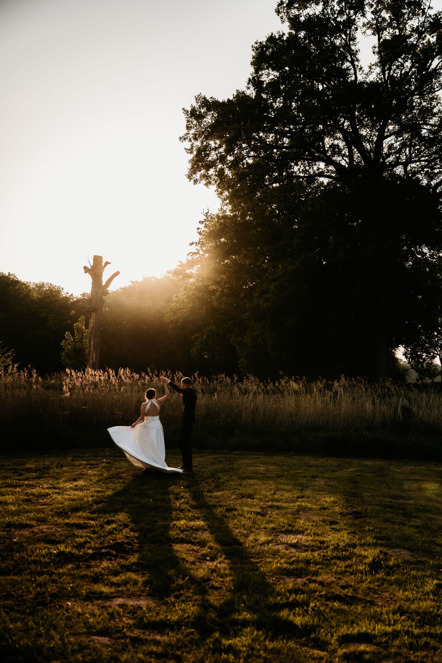 Silhouetted figures celebrating at sunset in a field with tall grass and trees.