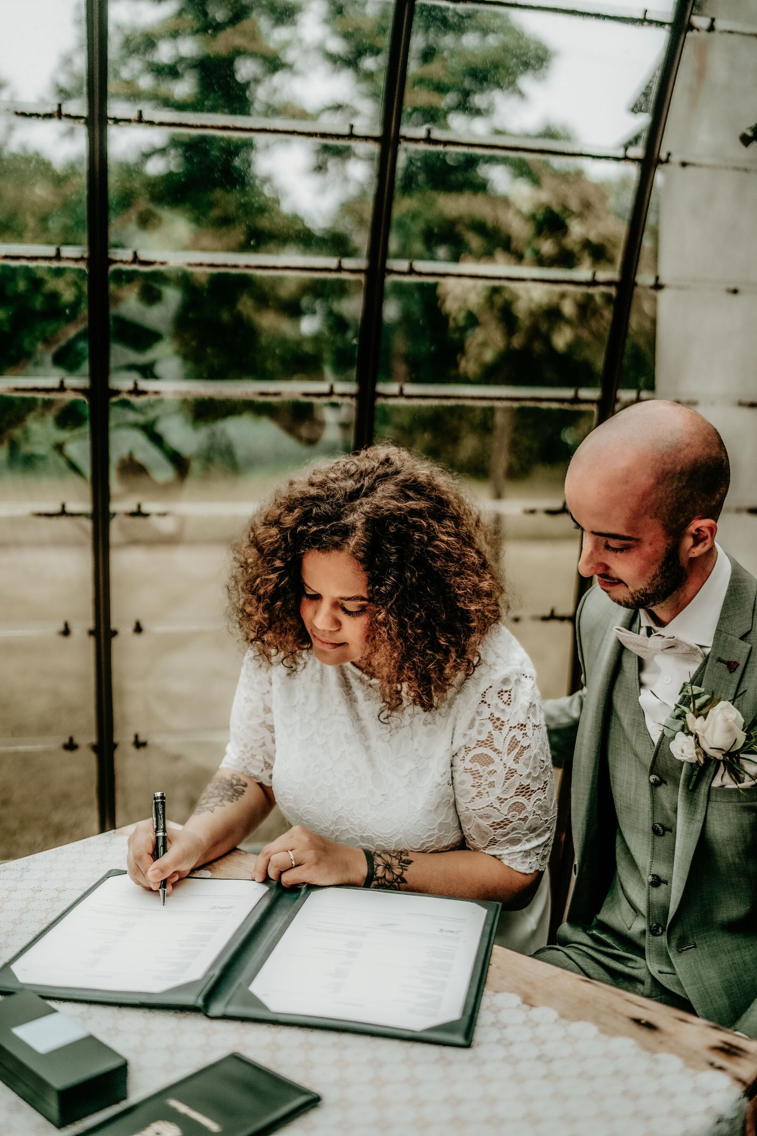 A couple signing marriage documents in a bright conservatory with glass ceiling.