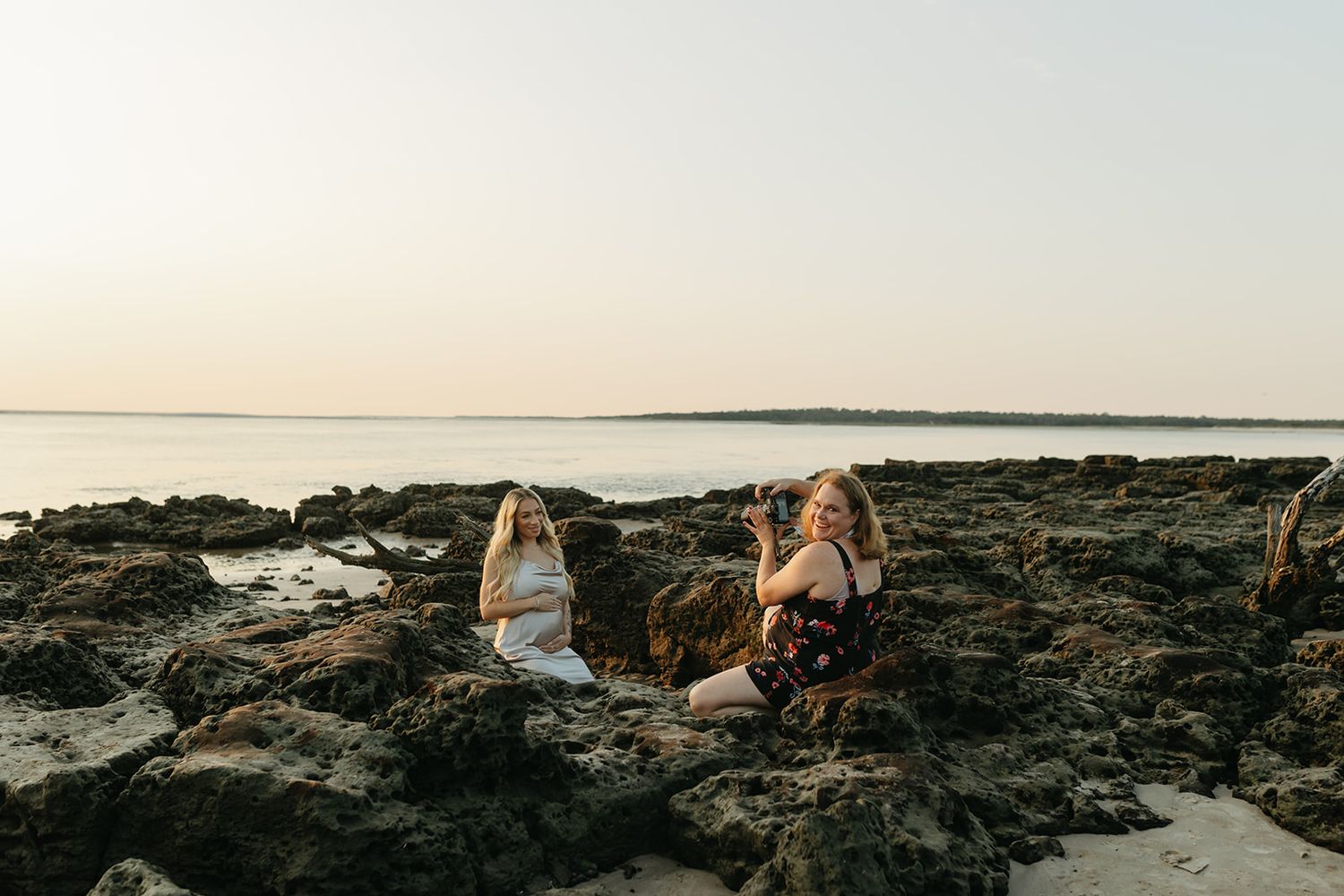 Dramatic sunset maternity photo session on rocky coastal shoreline.