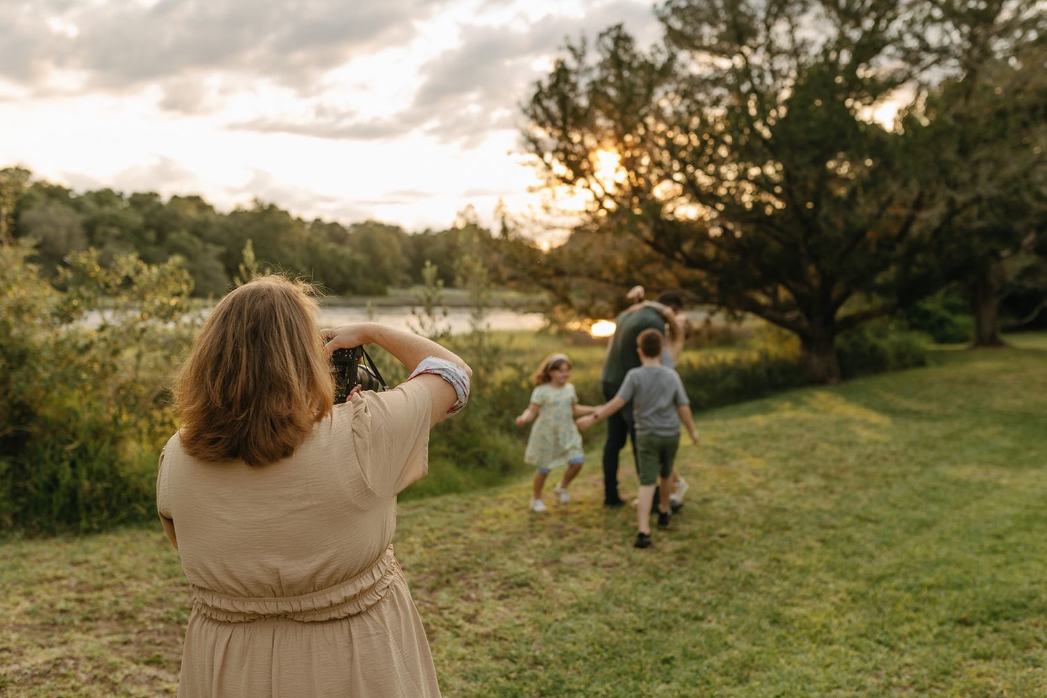 Jessica Life Jacksonville Family Photographer taking photos of others dancing in a scenic field at sunset.
