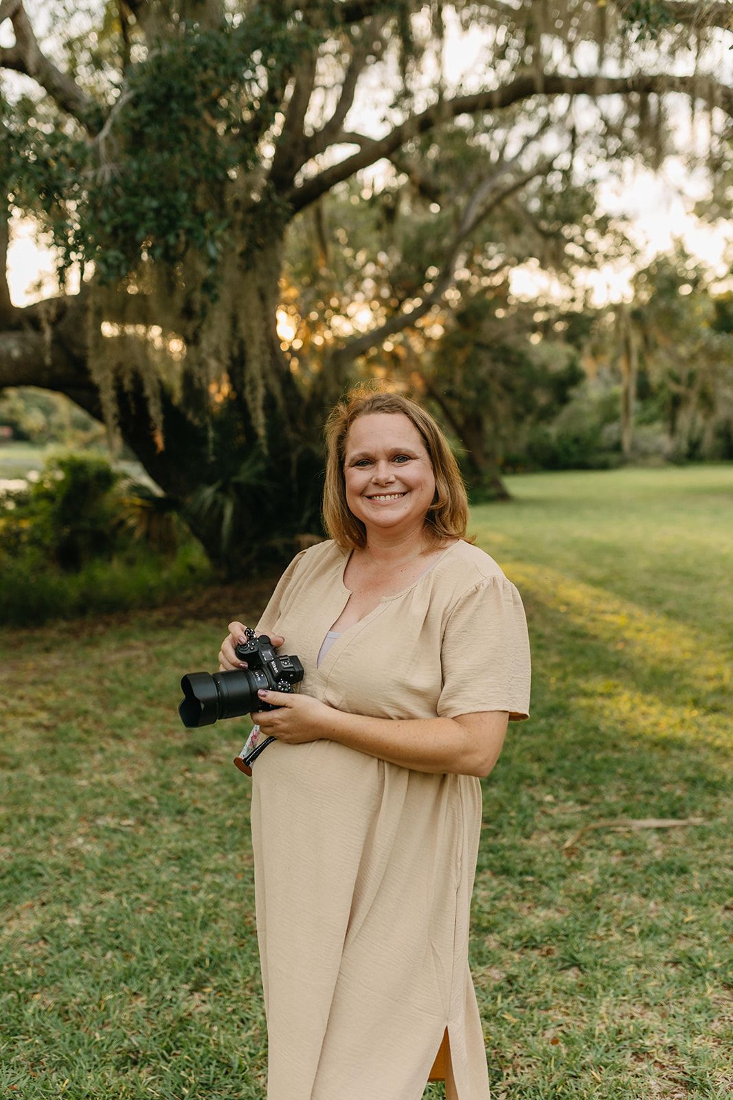 Professional photographer - Jessica Life Jacksonville Family Photography in beige dress holds camera while working outdoors.
