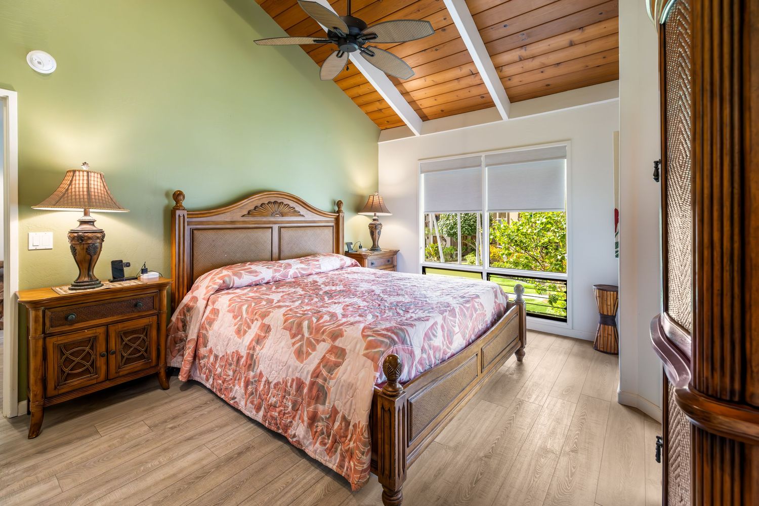 Spacious bedroom with wood ceiling and coral bedding in coastal style.