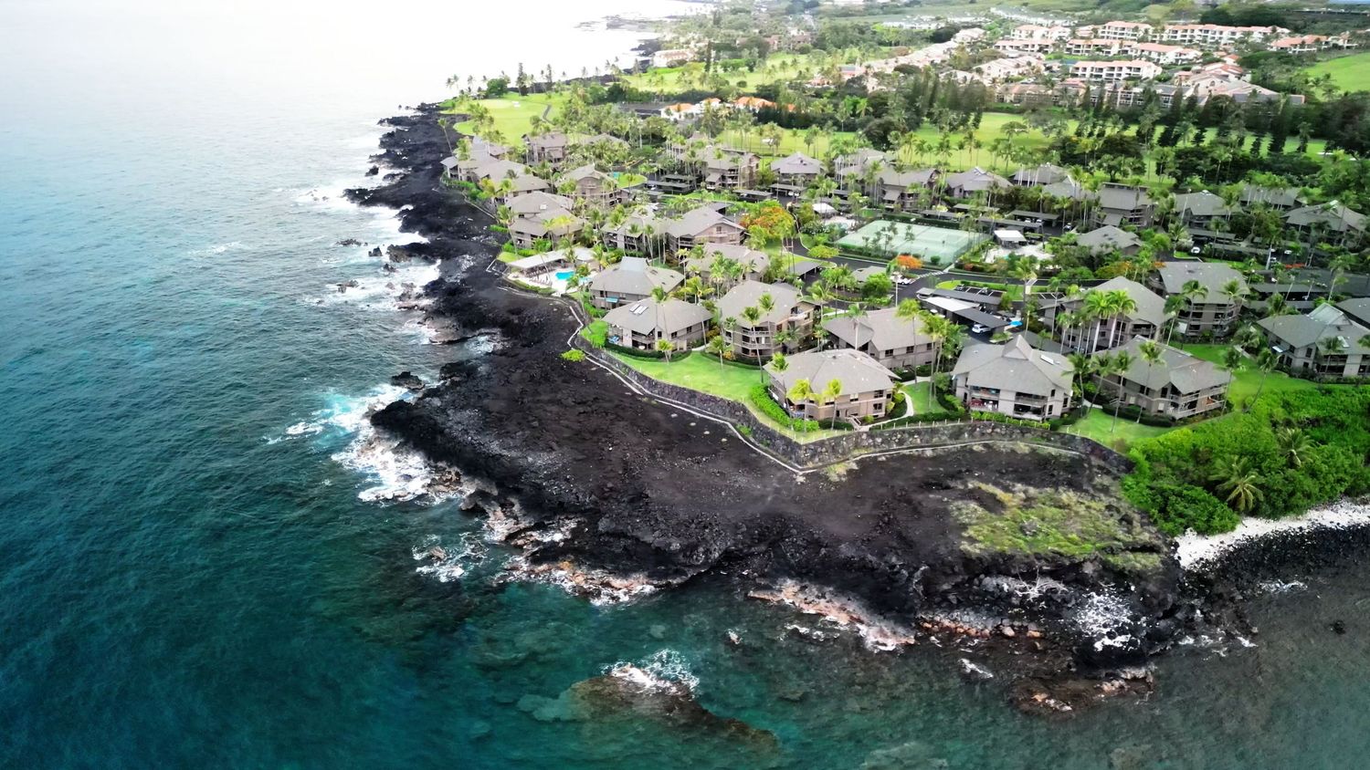 Aerial photograph of coastal homes built along volcanic shoreline in Hawaii.