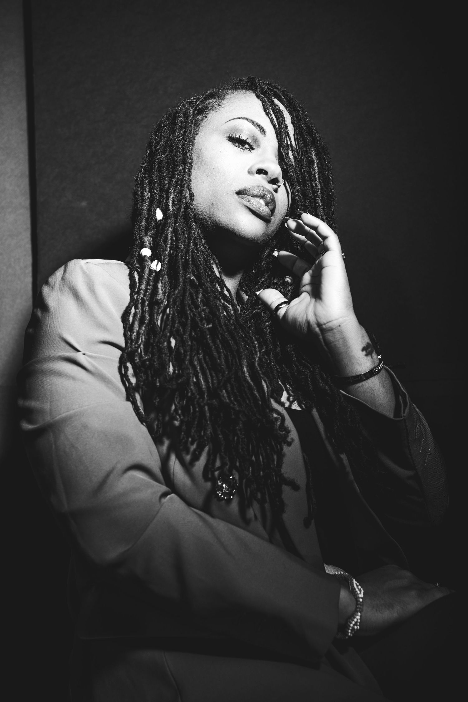 Moody portrait of someone with dreadlocks in blazer against dark background.