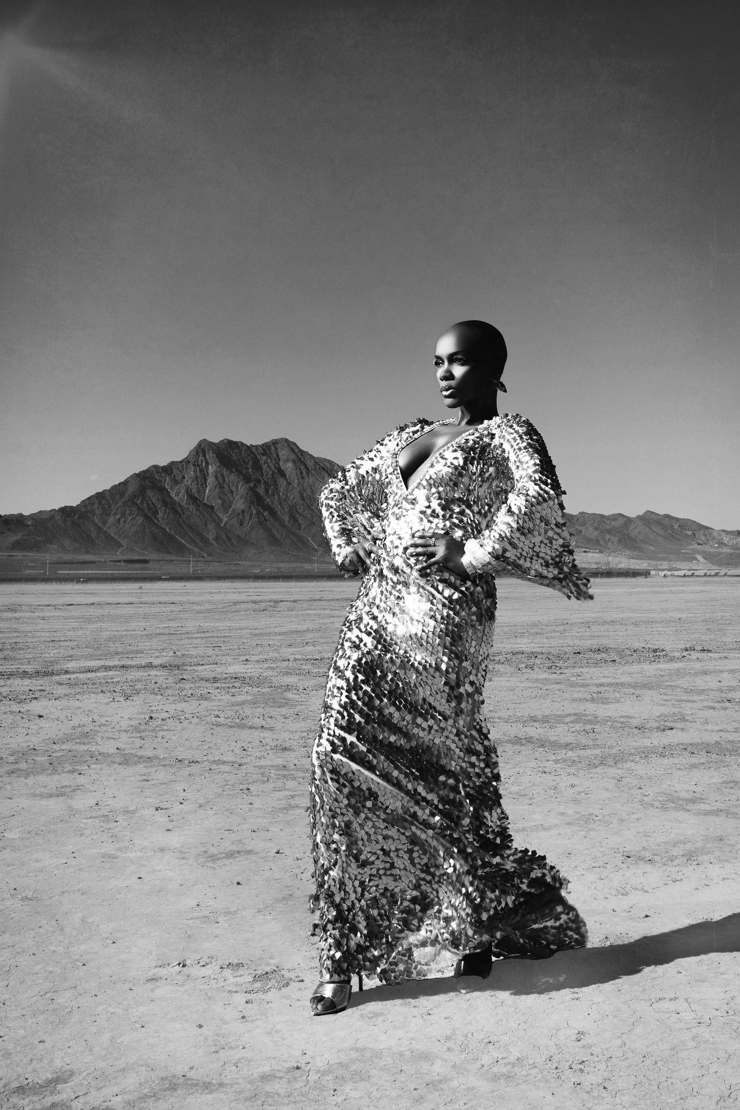 A striking black and white desert portrait of someone in a sequined gown with mountains in background.