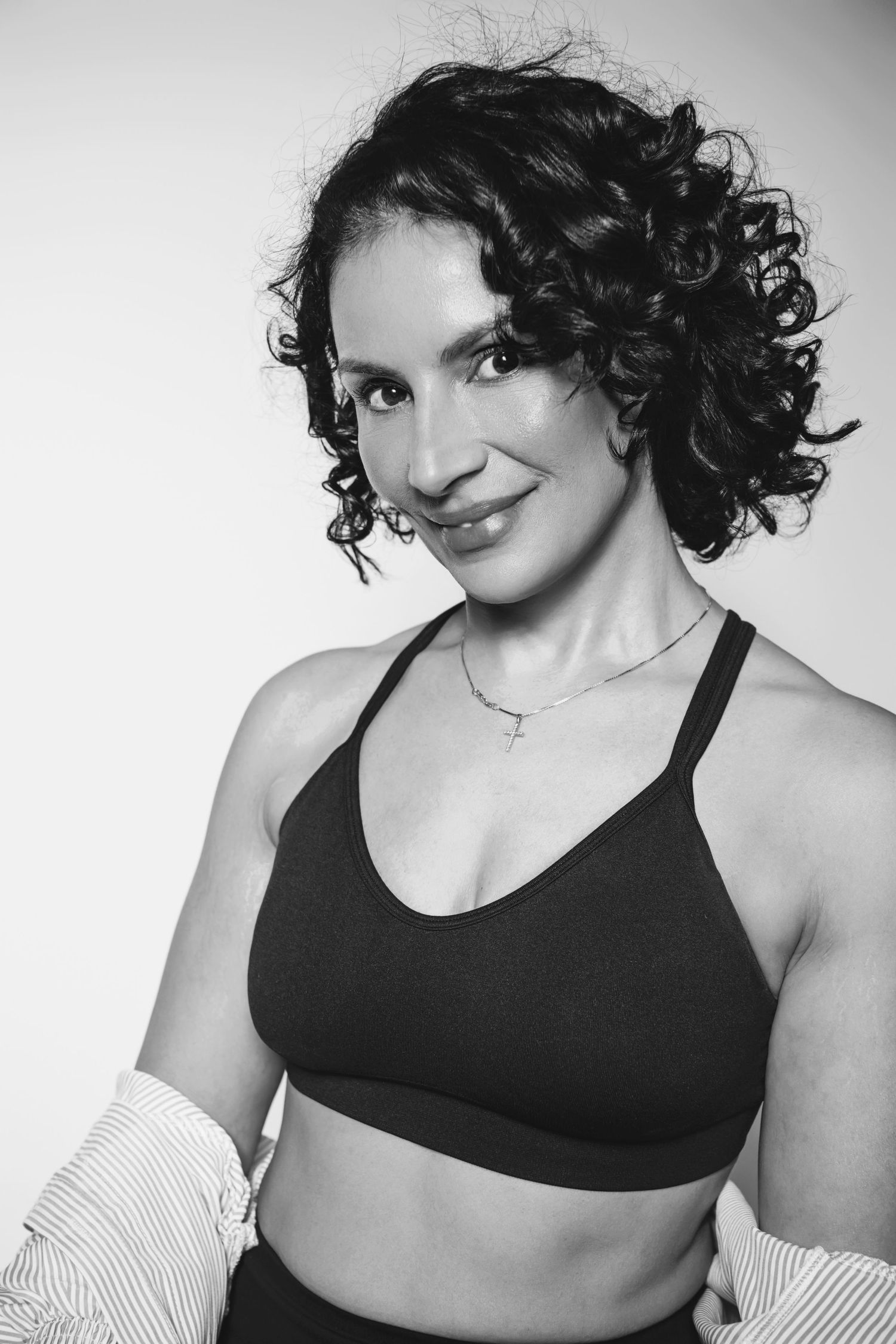 A black and white fitness portrait of someone with curly hair wearing athletic wear and smiling at the camera.