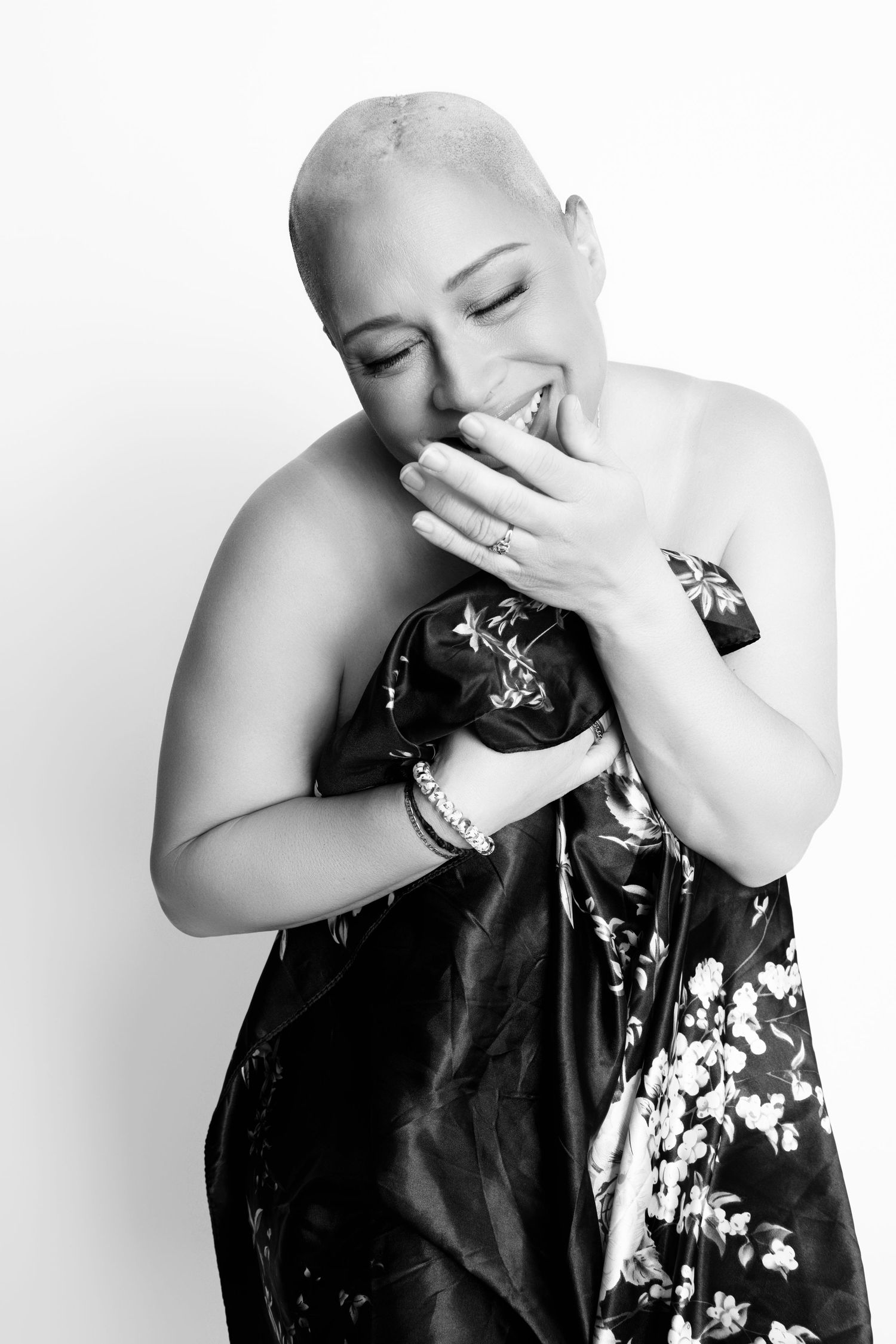 Joyful portrait of woman with shaved head wearing floral dress against white background.