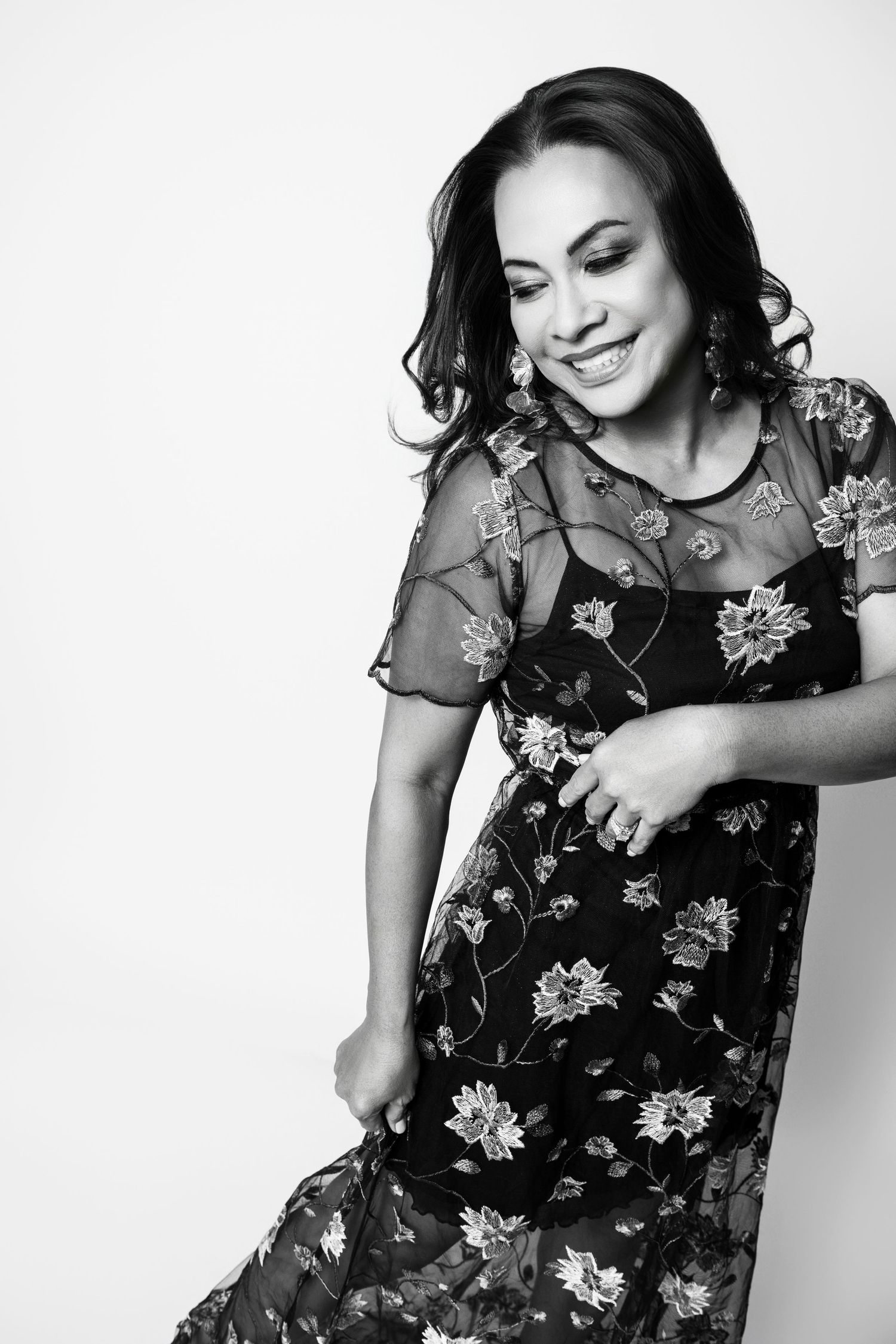 Woman in floral dress smiling and dancing against white background in black and white photo.